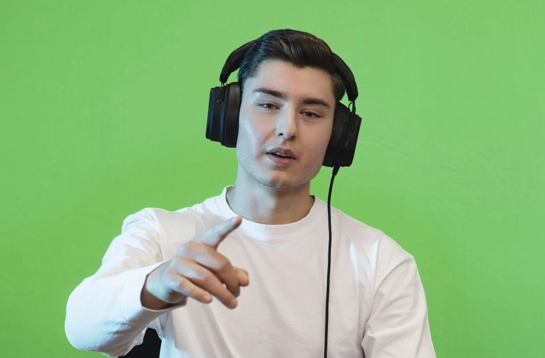 Młody mężczyzna ze słuchawkami wskazujący na kamerę na zielonym tle.