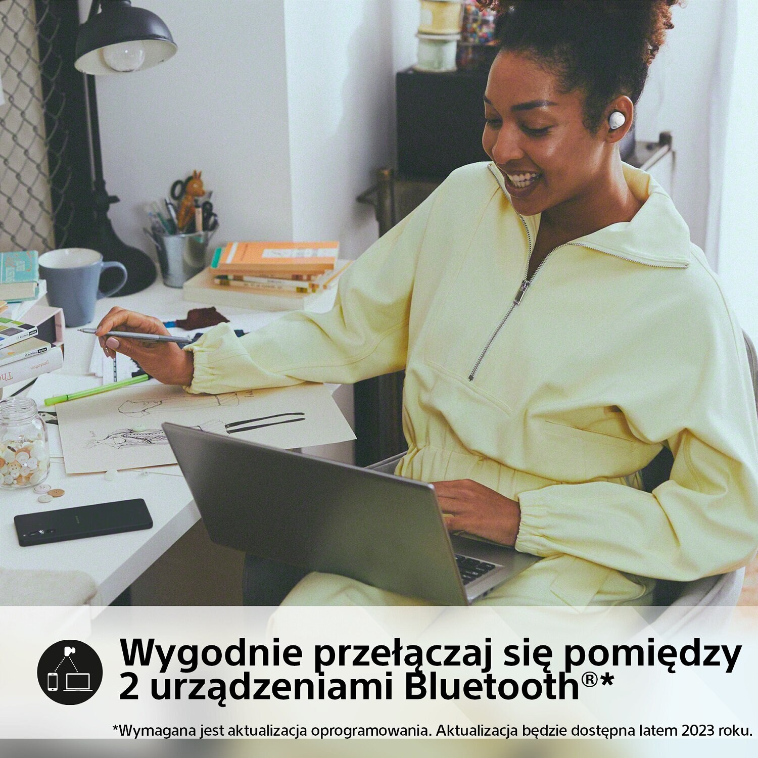 Kobieta pracuje przy biurku ze słuchawkami. W scenie jest laptop, kubek i długopis.