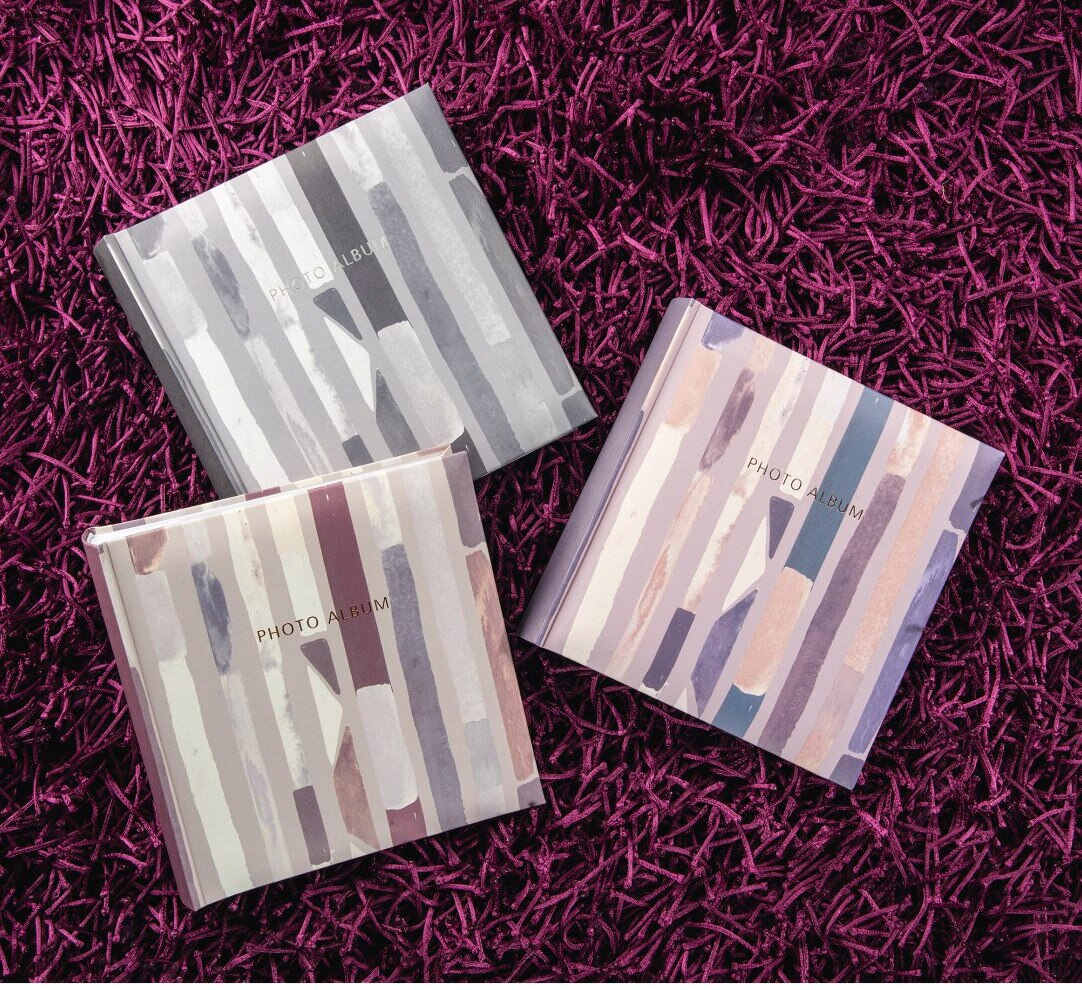 Trzy albumy ze zdjęciami z okładkami w stylu akwareli na fioletowym dywanie.