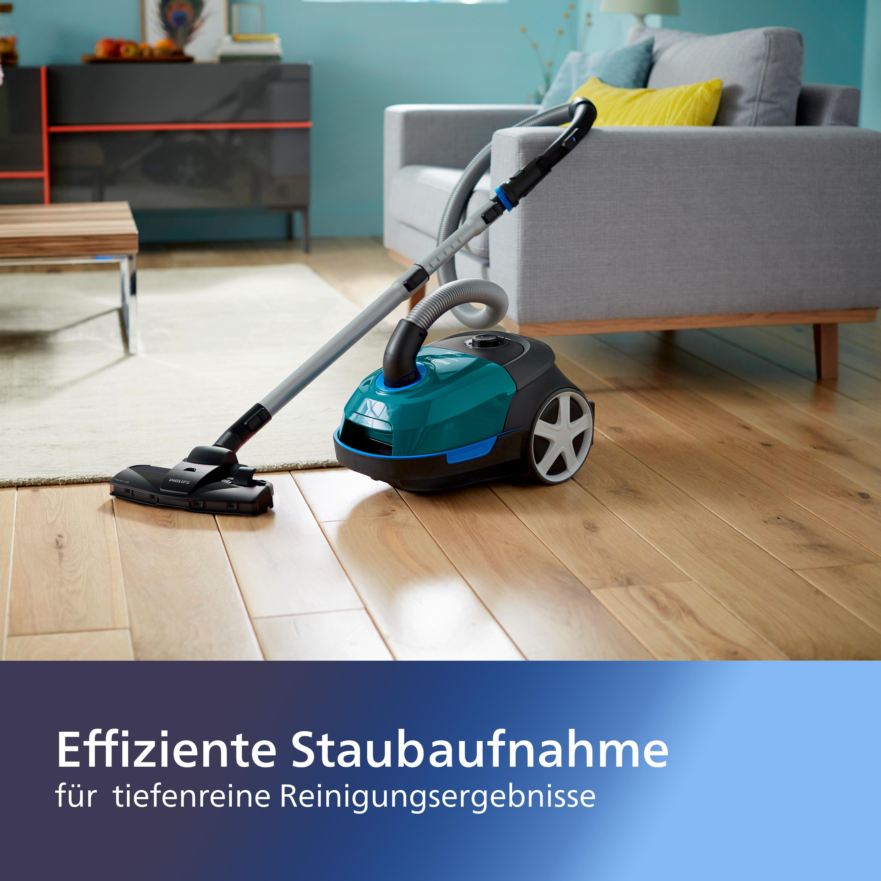 Staubsauger auf Holzboden, Text auf Deutsch, verschwommenes graues Sofa.