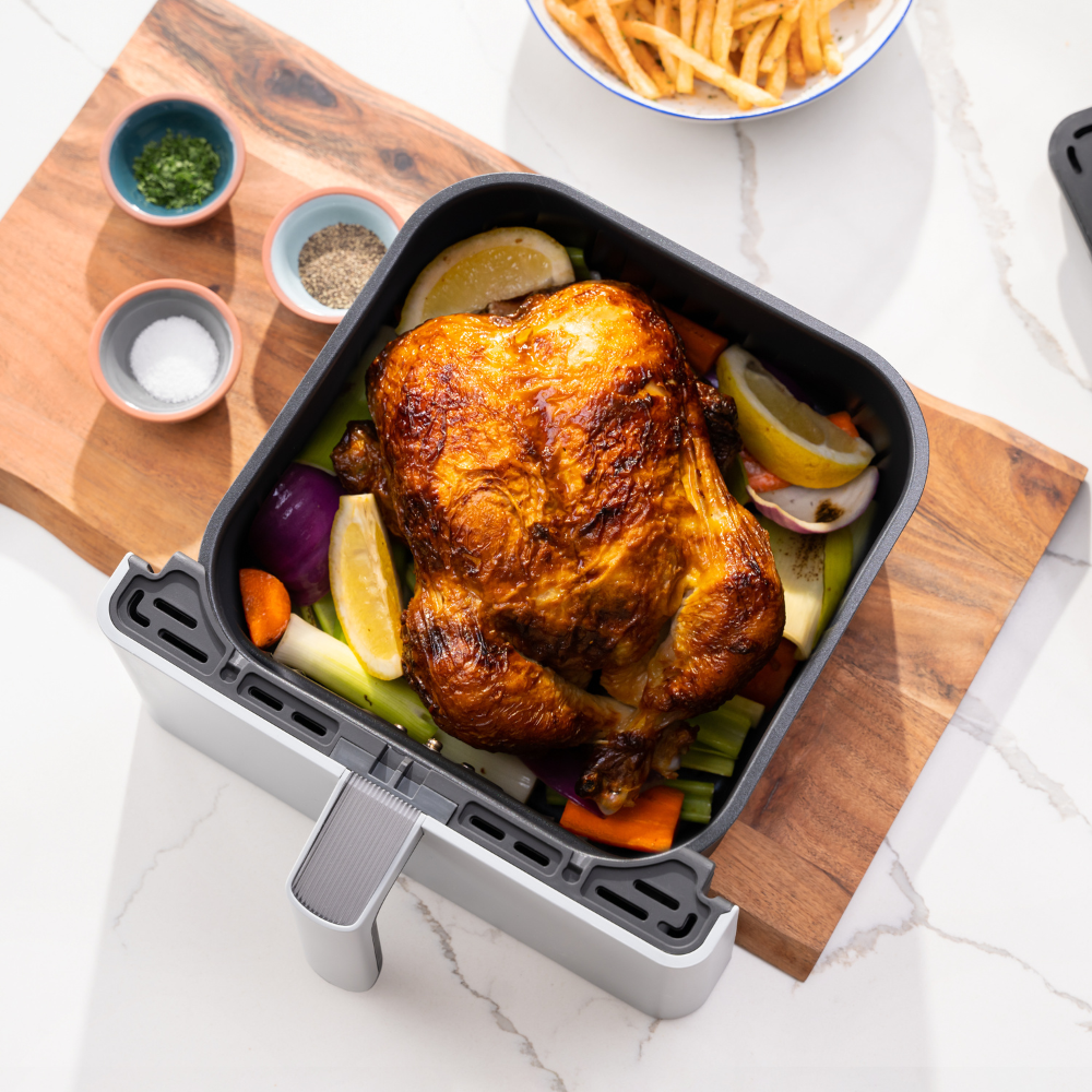 Freidora de aire con pollo y verduras cocinados, en tabla de madera, vista superior.