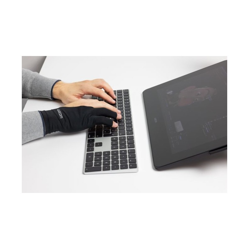 Manos tecleando en un teclado, una con un guante negro. Una tableta está al lado, mostrando una pantalla.