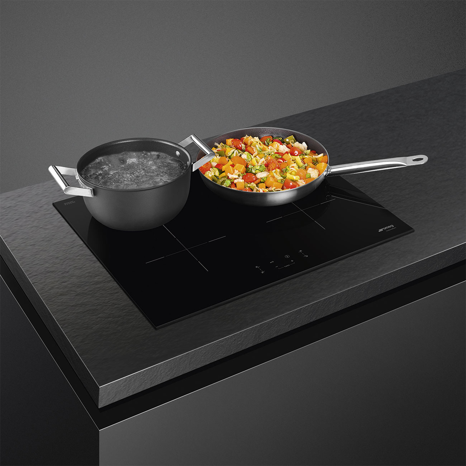 Piano cottura a induzione nero con una pentola e una padella che cucinano cibo. Piano di lavoro scuro.