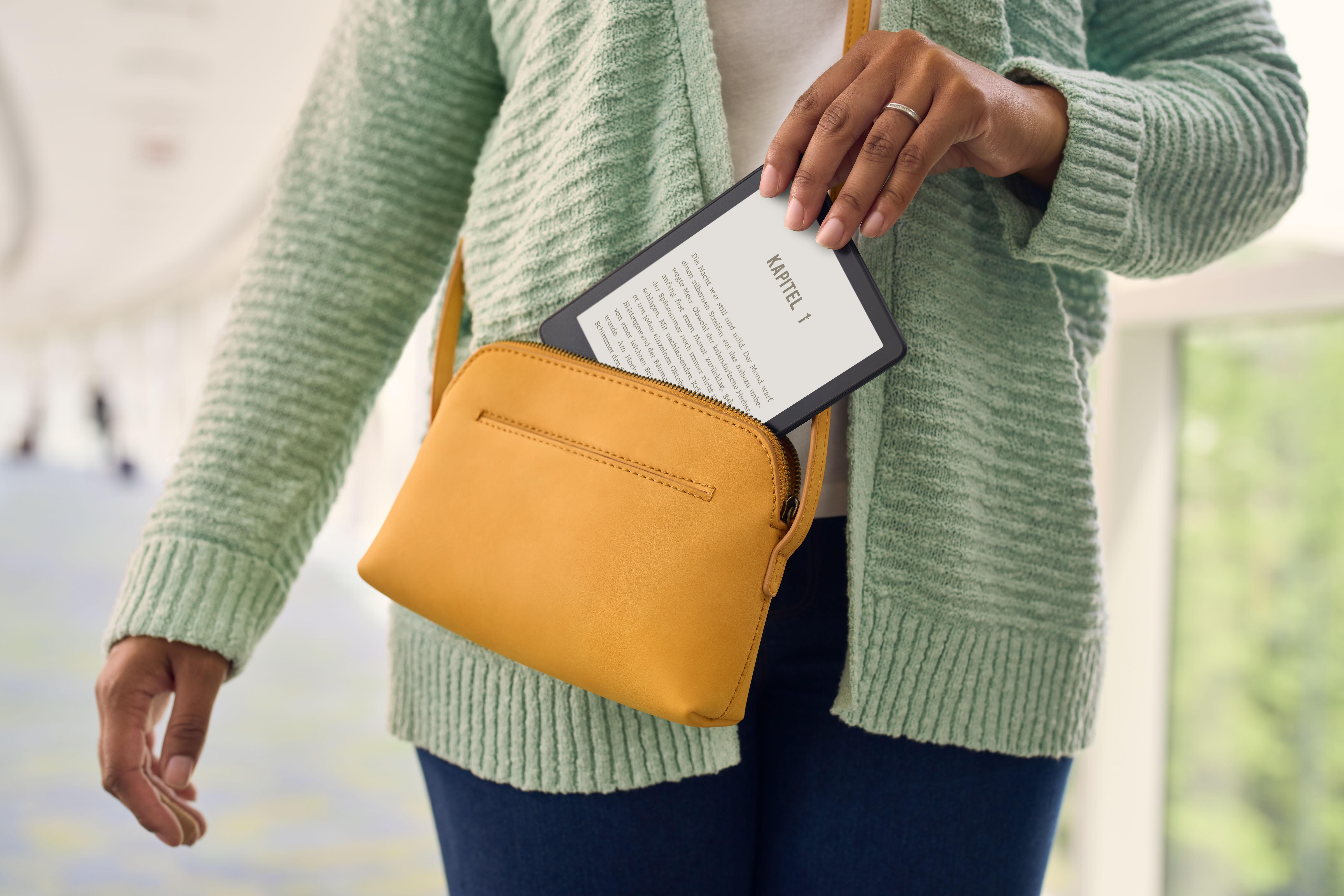 Eine Hand hält einen Kindle aus einer gelben Handtasche. Der Kindle zeigt Text auf Deutsch.