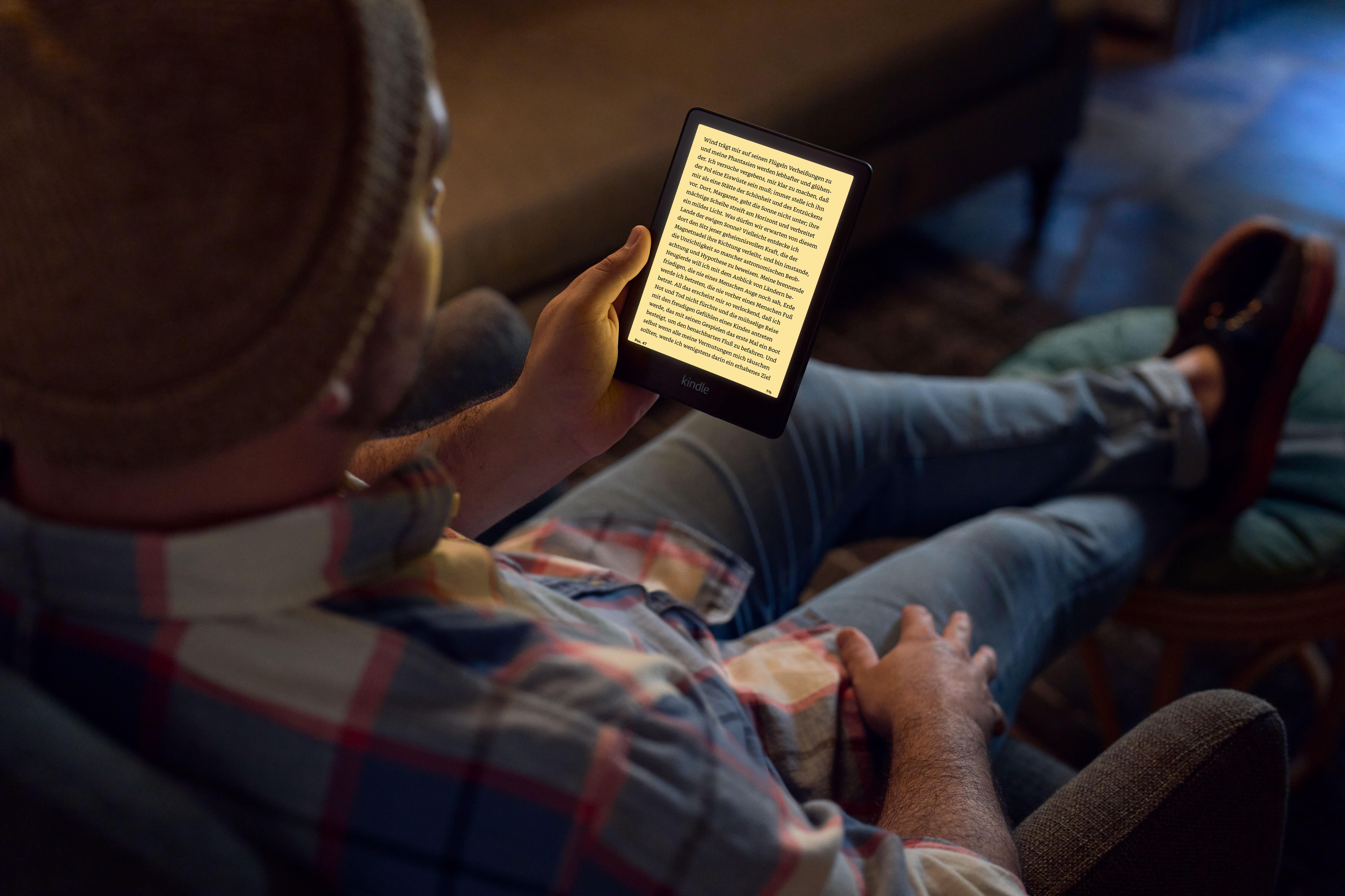 Eine Person mit Hut liest einen Kindle-E-Reader, während sie auf einer Couch sitzt.