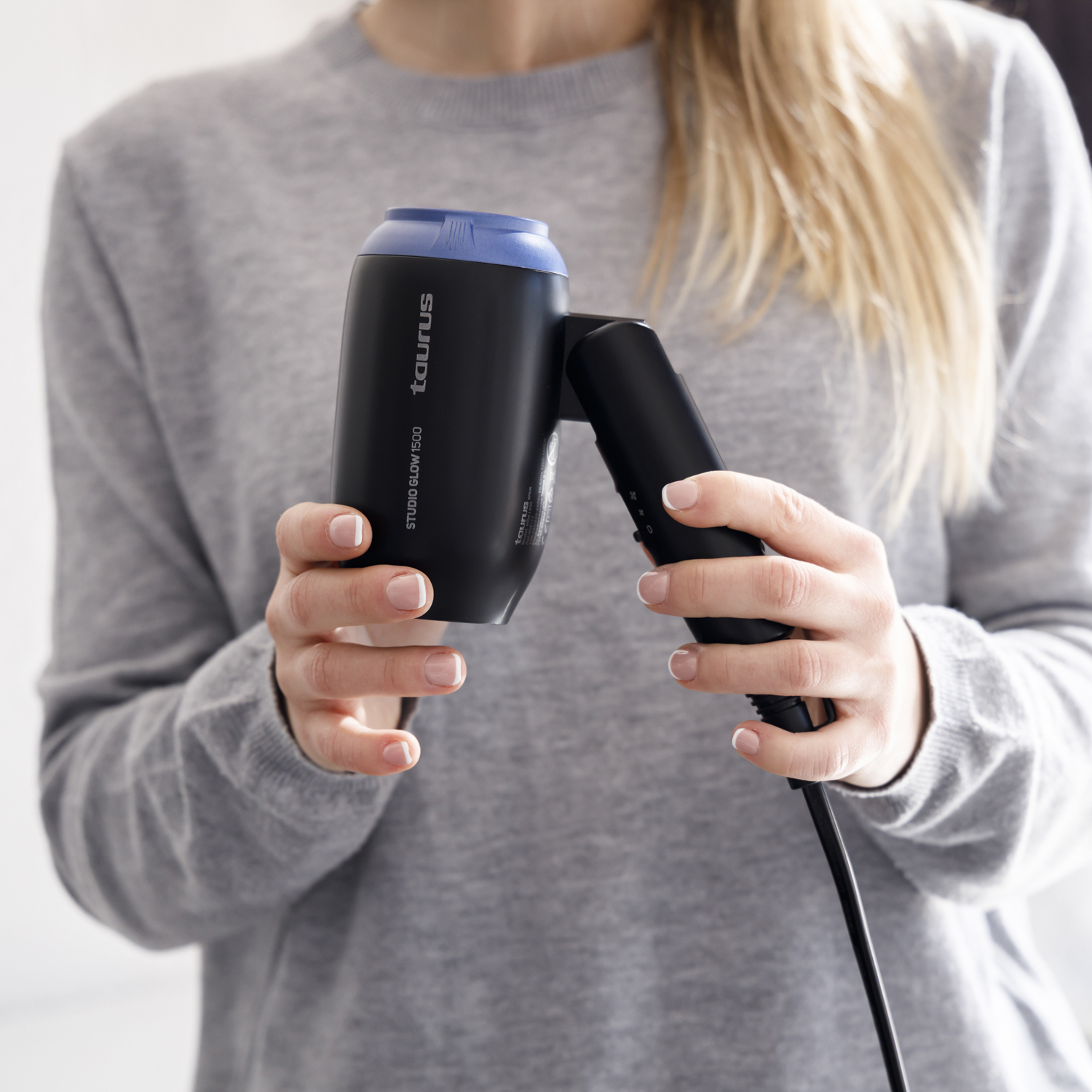Mujer sosteniendo un secador de pelo negro y azul, modelo Taurus Studio Glow 1500.