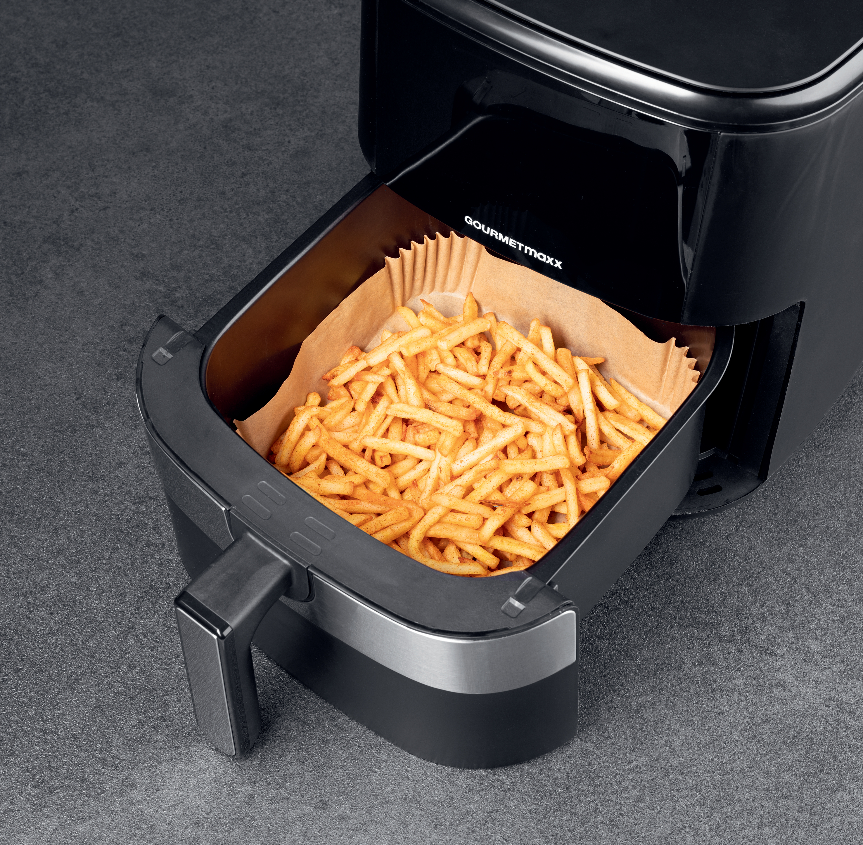 Schwarzer Frittierkorb gefüllt mit goldenen Pommes Frites, in dem Gerät, mit grauem Hintergrund.