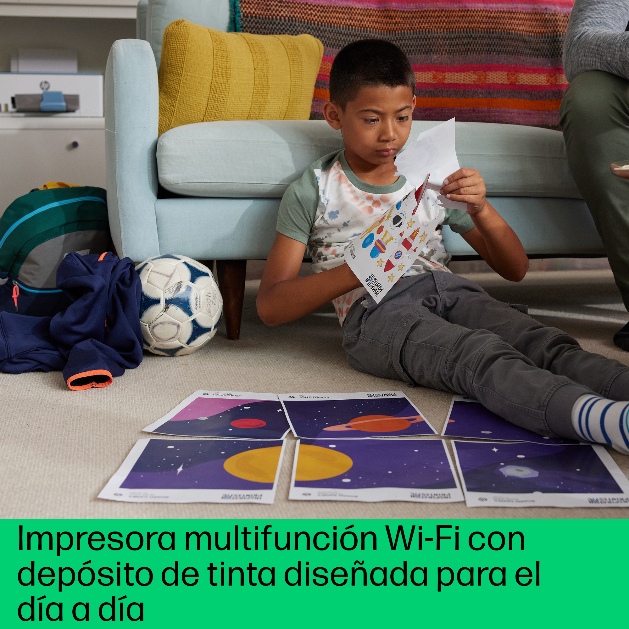 Niño mirando papeles en el suelo. Hay un balón de fútbol, sofá e impresora.