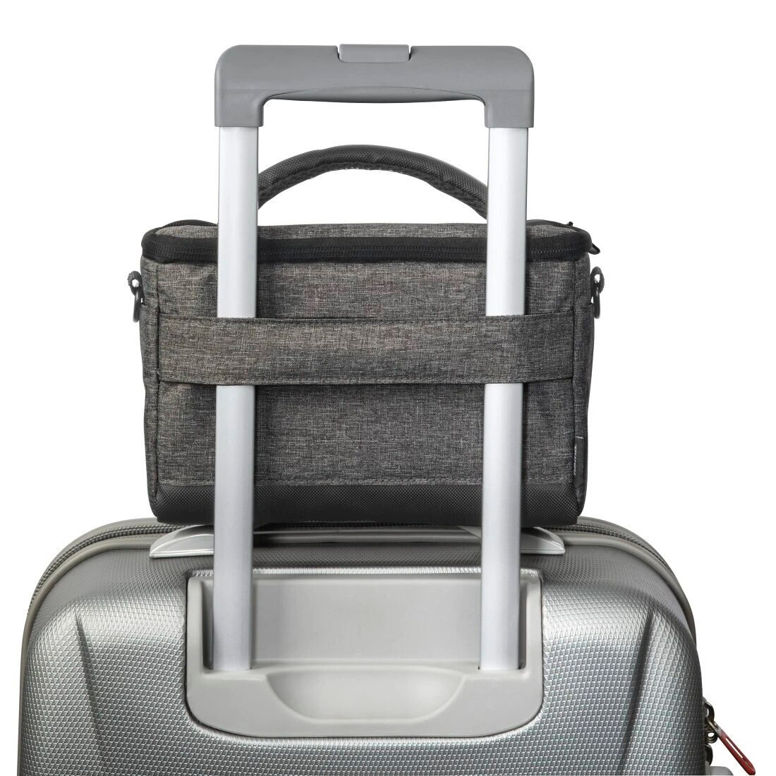 Szara torba na aparat spoczywająca na srebrnym uchwycie walizki. Białe tło.