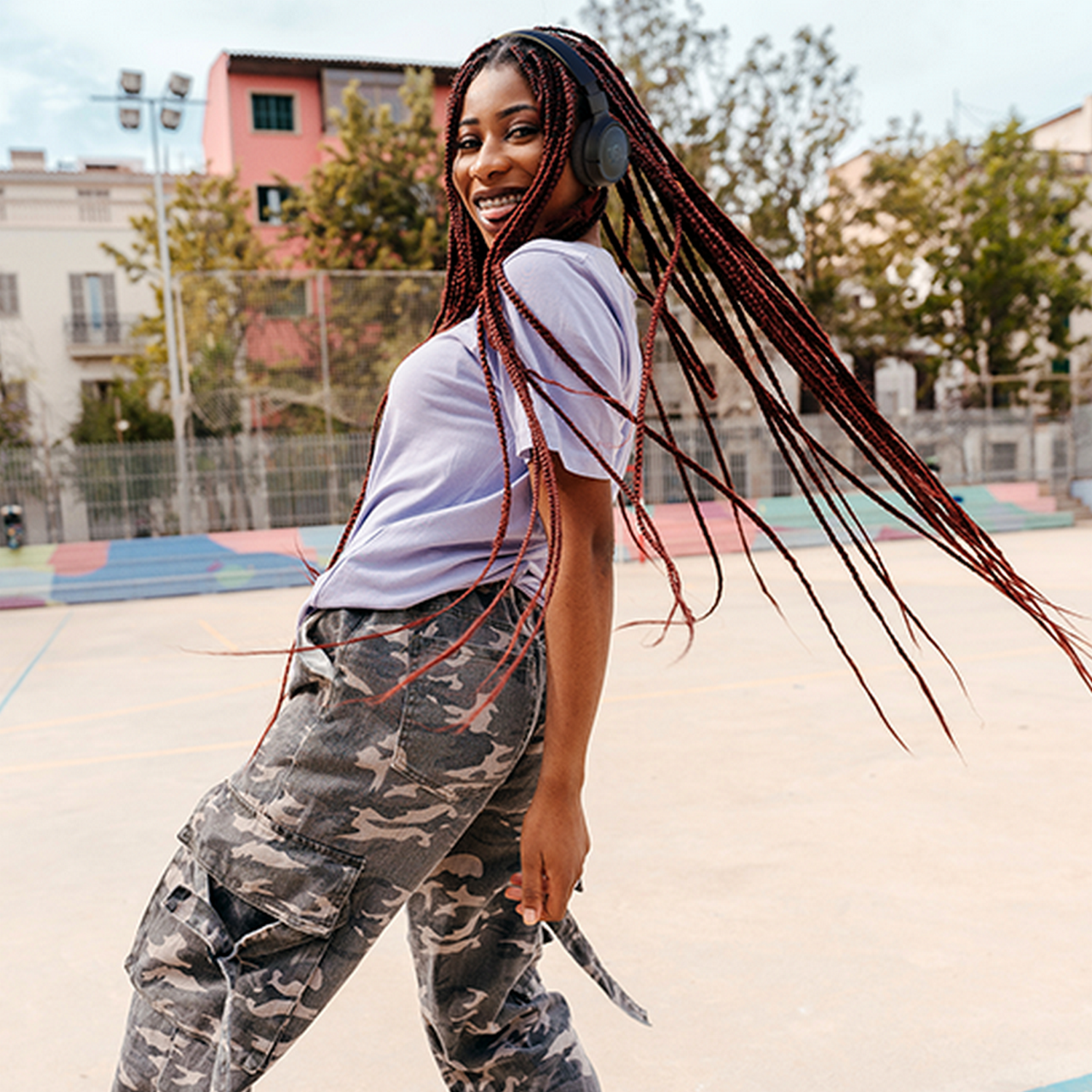 Young woman with long braids and headphones, wearing camo pants and a purple top.