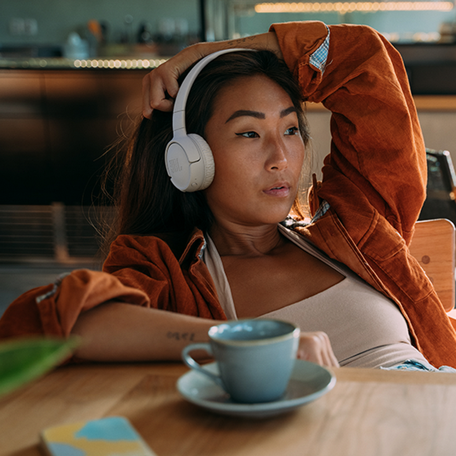 Aziatische vrouw met een koptelefoon en een kop koffie op een tafel.