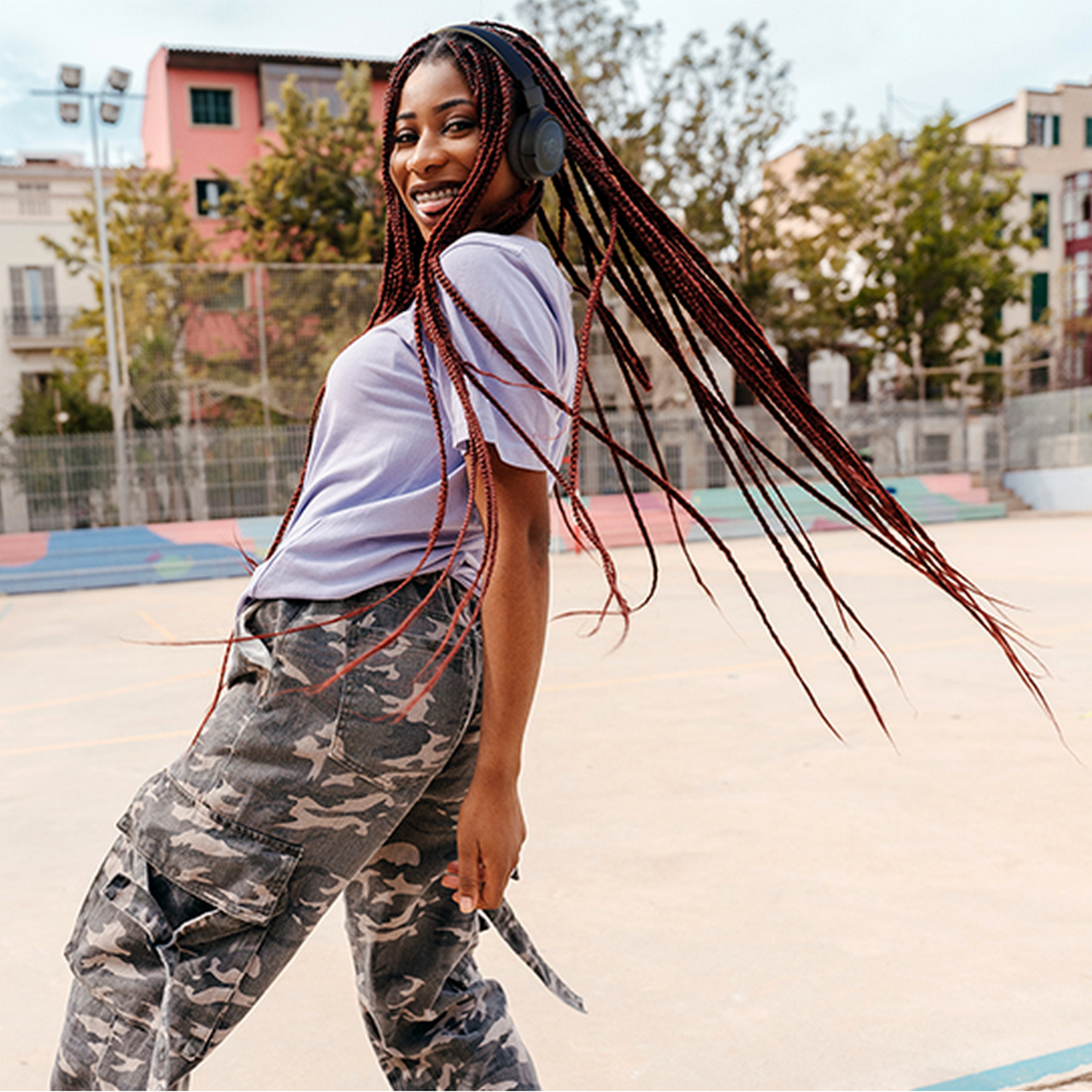 A smiling woman with braids and headphones, in front of a city background.