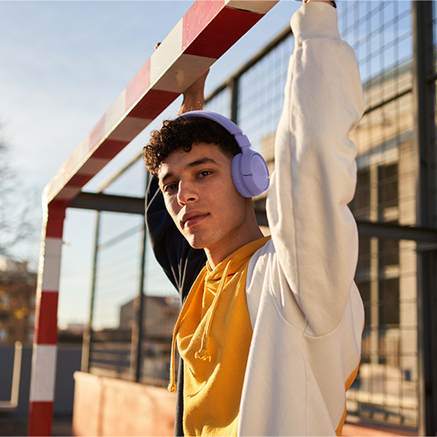 A young man wearing purple headphones, standing near a red and white goal, looking at the camera.