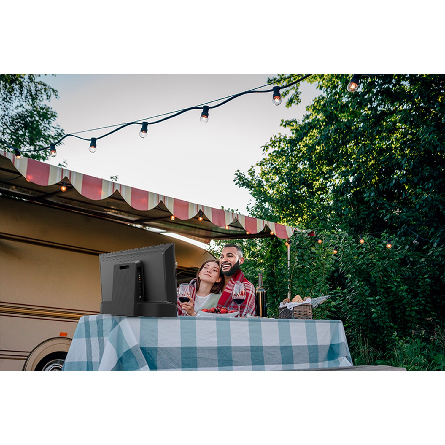 Koppel geniet van wijn en eten aan een tafel buiten een camper bij zonsondergang.