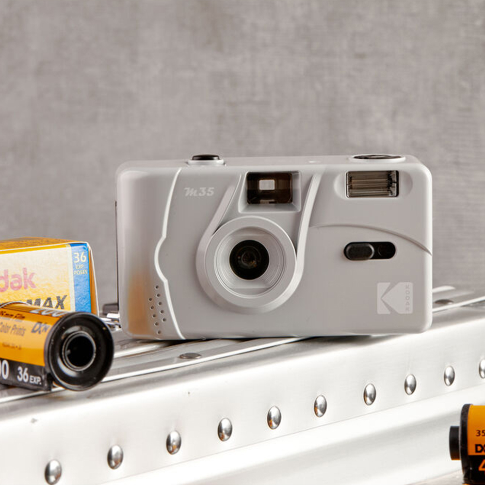 Egy szürke Kodak M35 filmes fényképezőgép, filmtekercsekkel. A kamera fókuszban van.