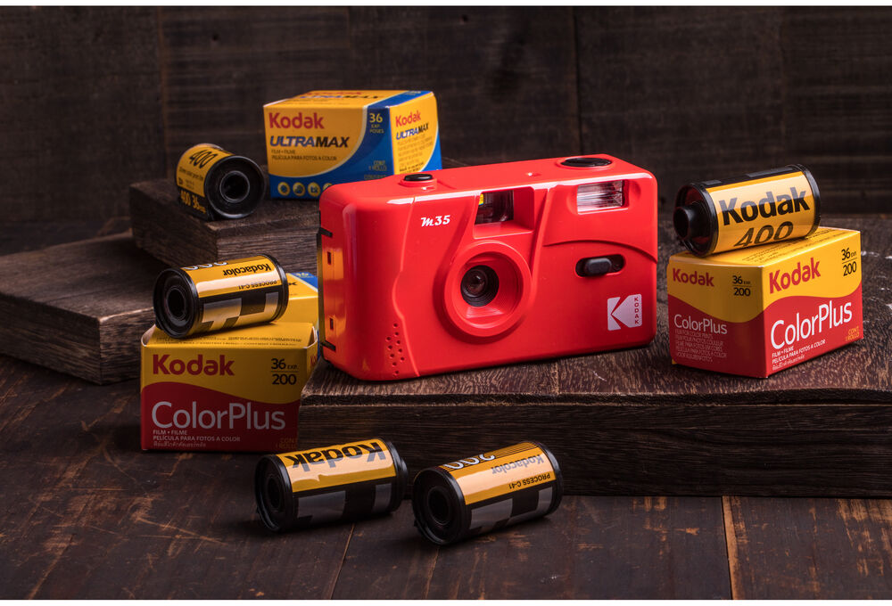 Piros Kodak M3.5 kamera több filmtekercsel fa tömbökön. Film dobozok és tekercsek láthatók.