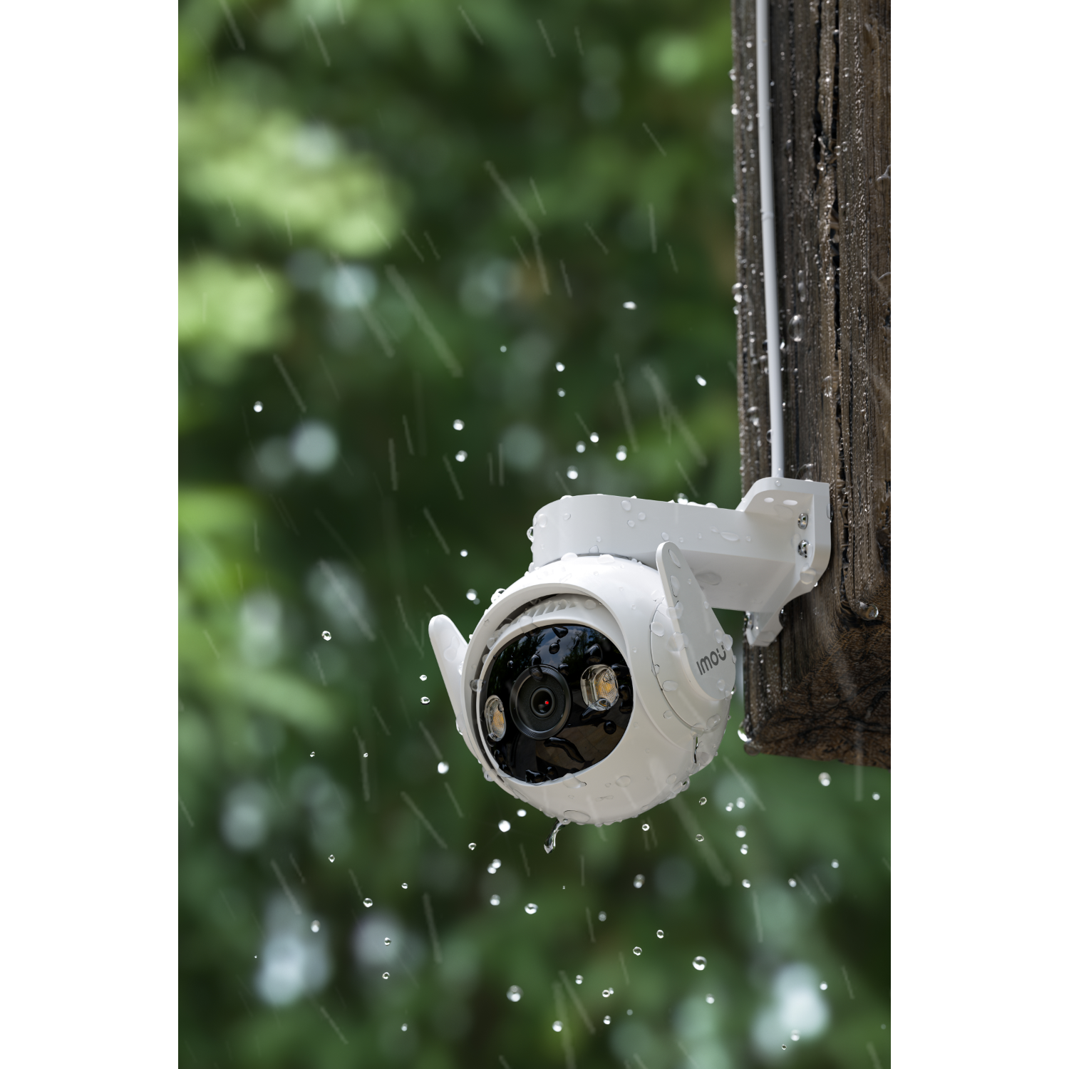 A white security camera mounted on a wooden post. Rain falls around it. The camera has a black lens.