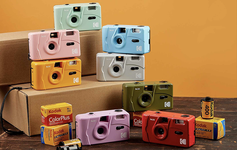 Színes Kodak fényképezőgépek és filmdobozok gyűjteménye fa felületen.