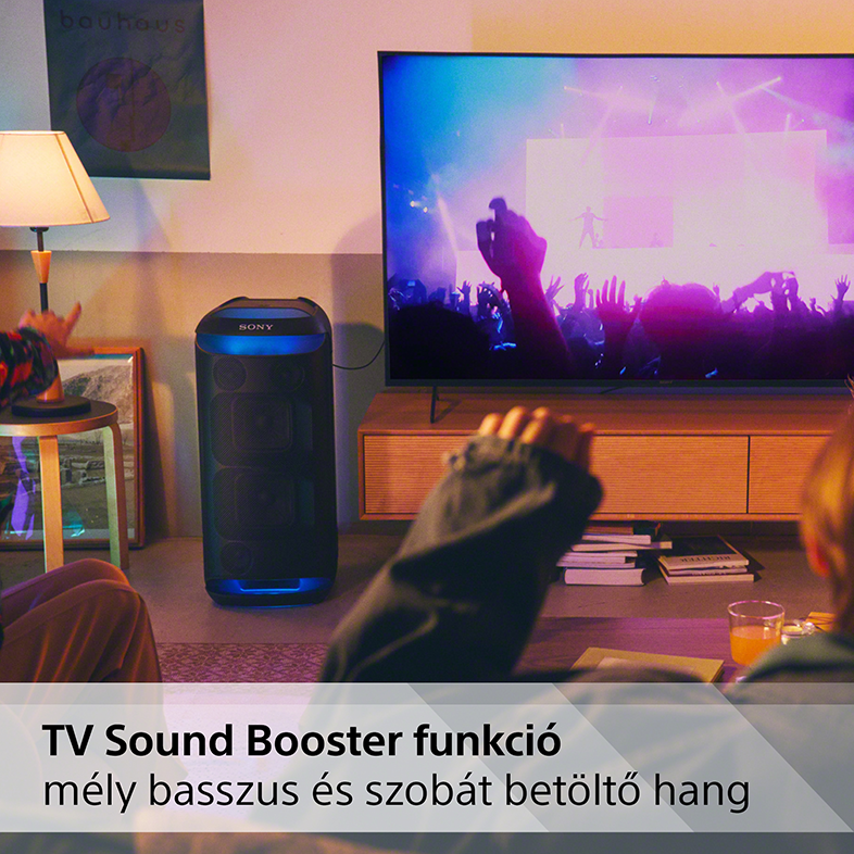 Egy nappali jelenet tévével, hangszóróval és emberekkel, akik a képernyőt nézik.