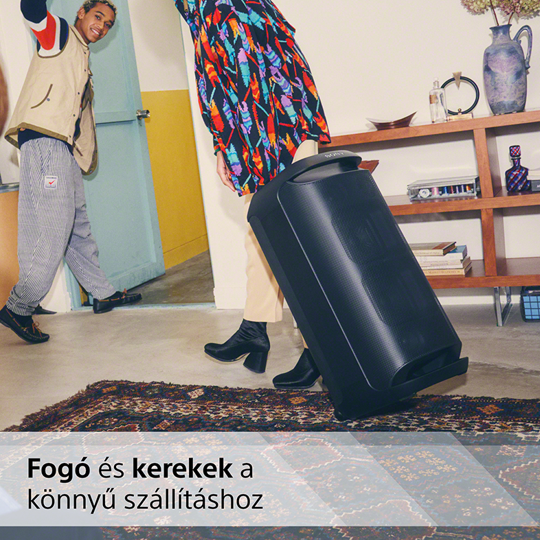 Két ember egy hangszóróval. Az egyik hordja, a másik a szőnyegen jár.