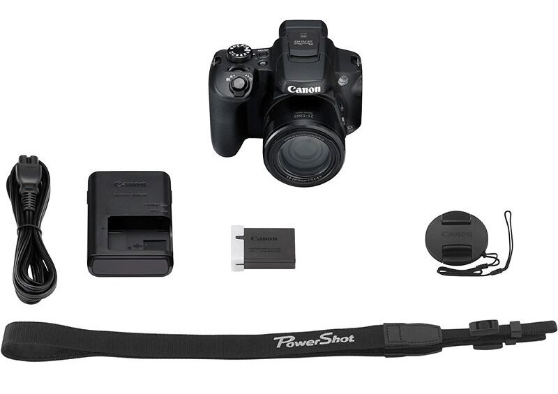 Aparat z akcesoriami: ładowarka, bateria, pasek i osłona obiektywu. Wszystkie przedmioty są czarne.