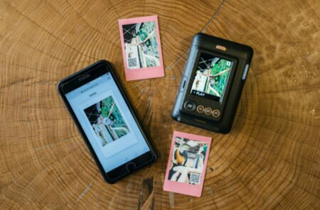 Drewniany stół ze smartfonem, dwoma zdjęciami i aparatem natychmiastowym z ekranem.