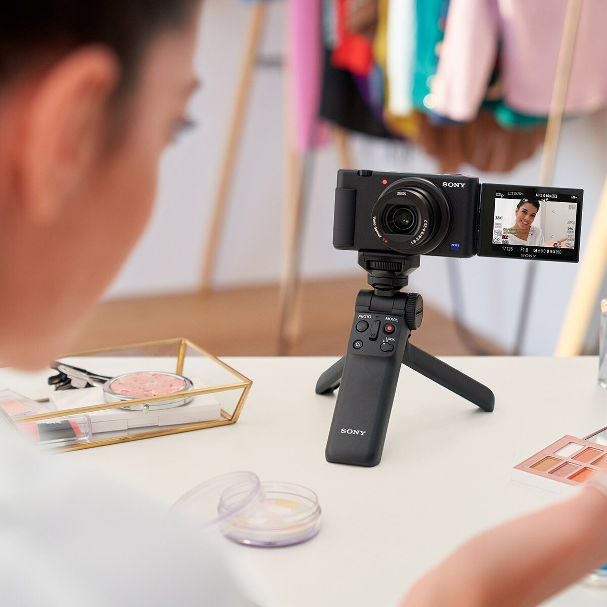 Kobieta filmuje kamerą Sony na statywie, z makijażem i innymi przedmiotami na stole.