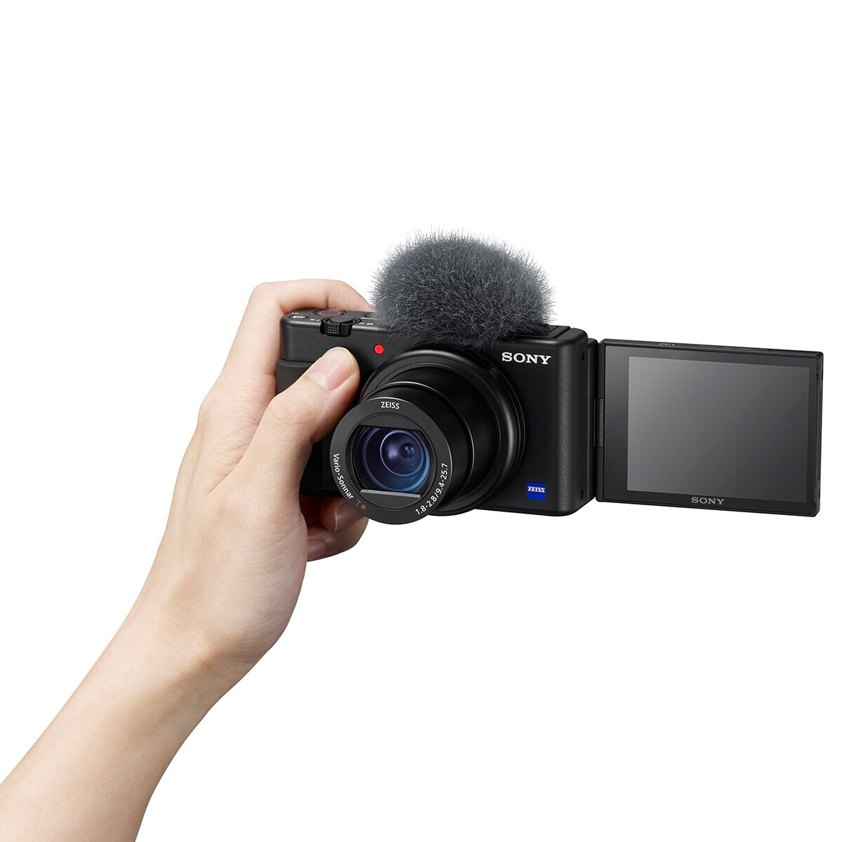 Ręka trzyma czarną kamerę Sony z mikrofonem, otwartym ekranem. Białe tło.