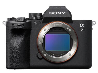 Czarny aparat Sony Alpha 7 z dołączonym obiektywem na białym tle. Widoczny srebrny pierścień obiektywu.