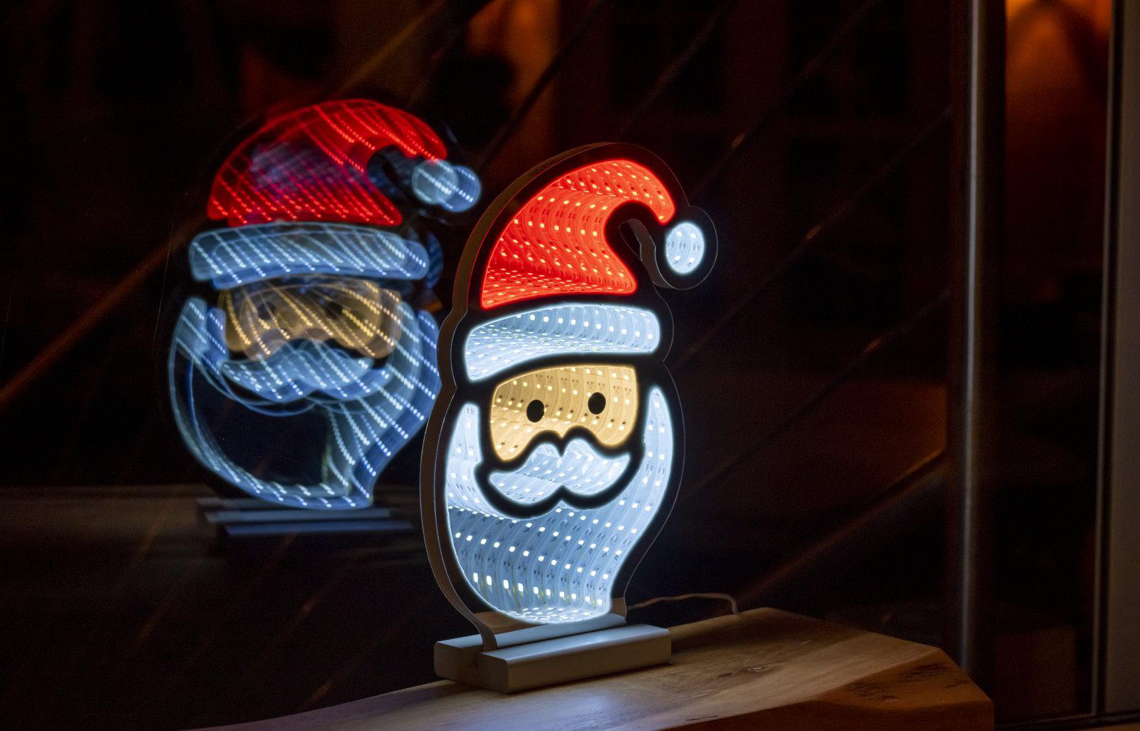 Weihnachtsmann-Lichtdekoration mit Spiegelung auf einer Holzoberfläche.