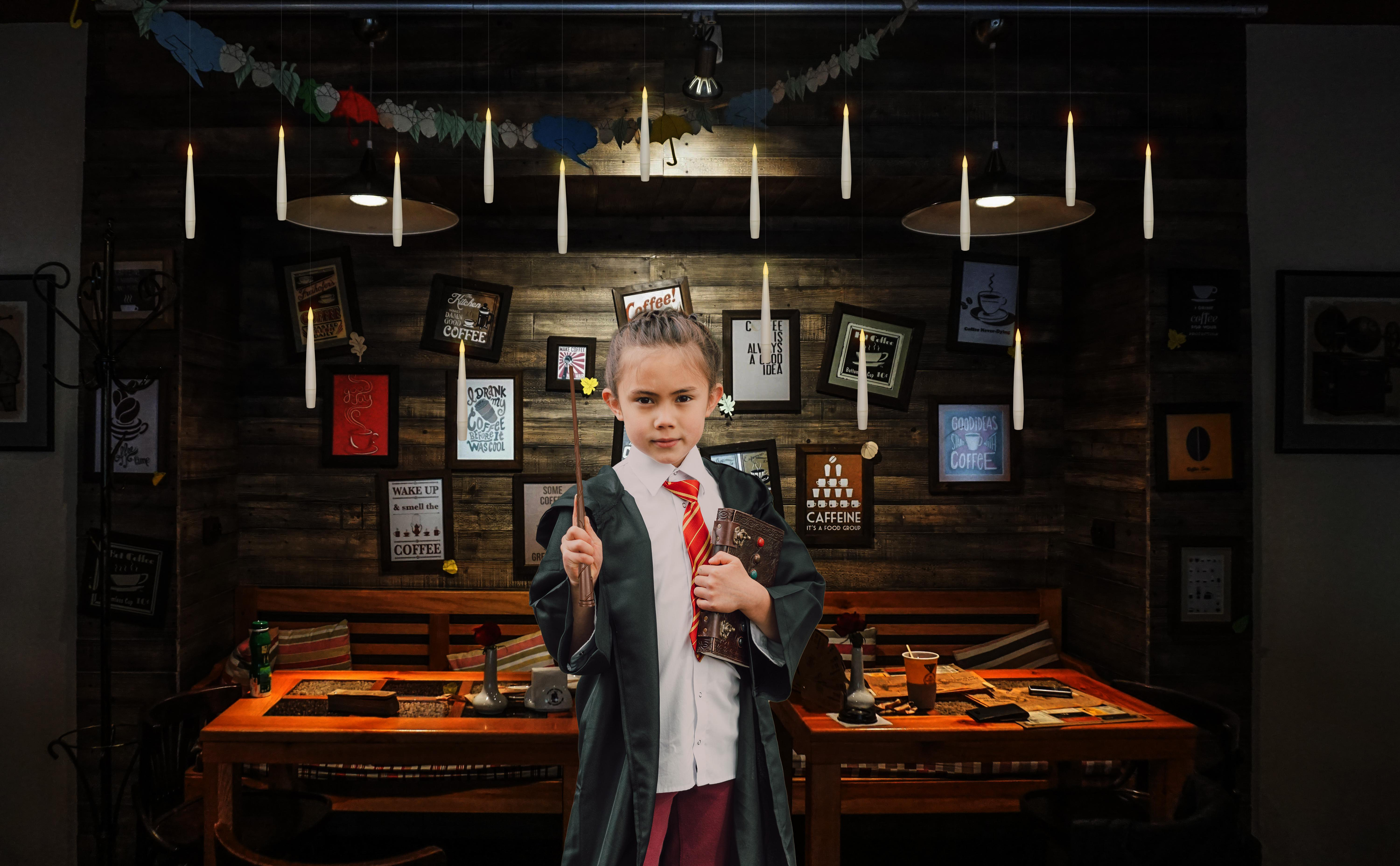 Junges Mädchen in Harry-Potter-Robe hält Zauberstab und Buch in einem Café.