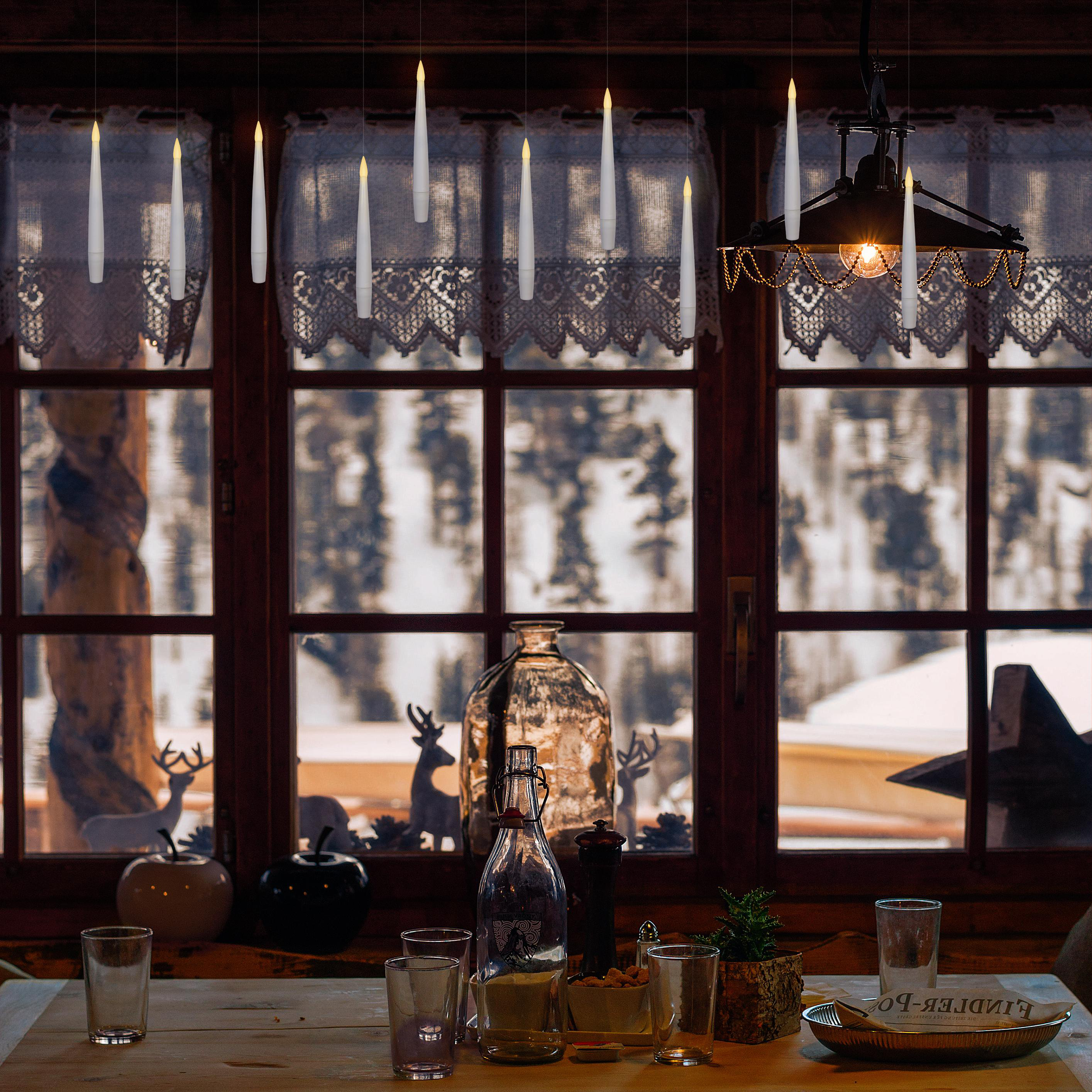 Innenraum mit Kerzen in der Nähe eines Fensters, Tisch mit Gläsern und einer Flasche.