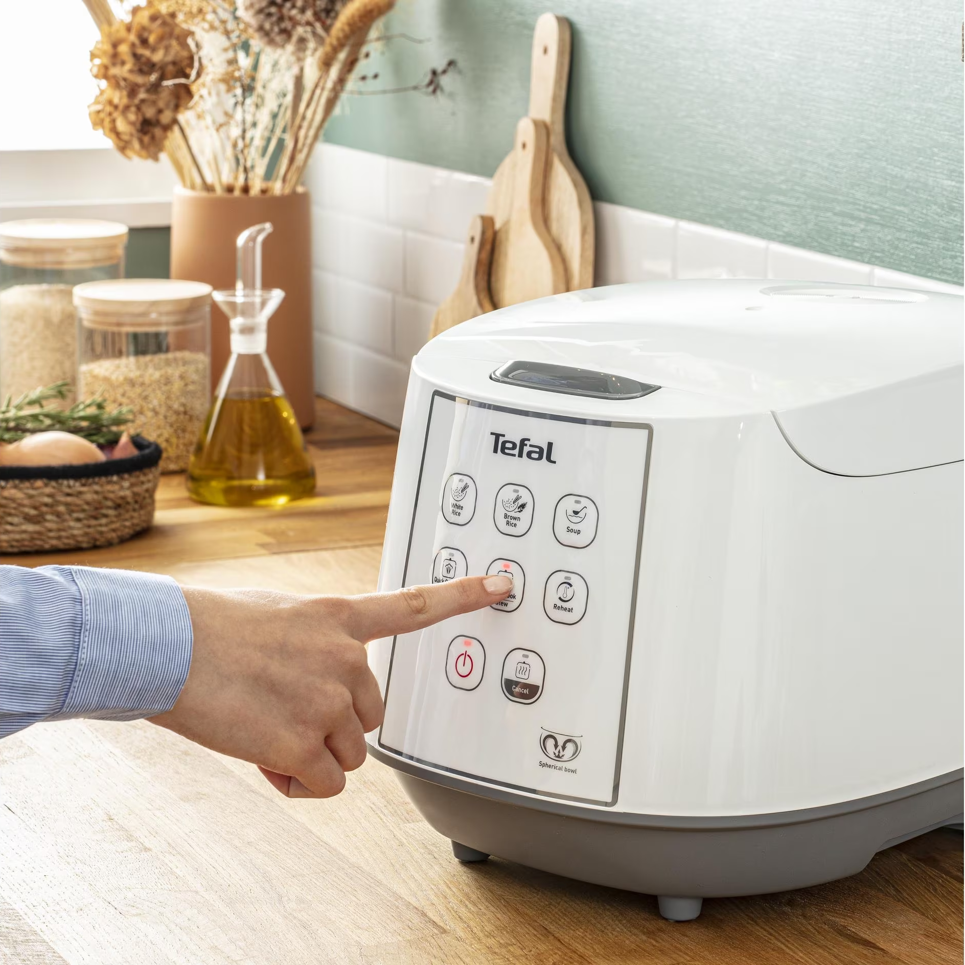 Eine Hand drückt auf eine Taste eines weißen Tefal-Reiskochers. Andere Elemente sind vorhanden.