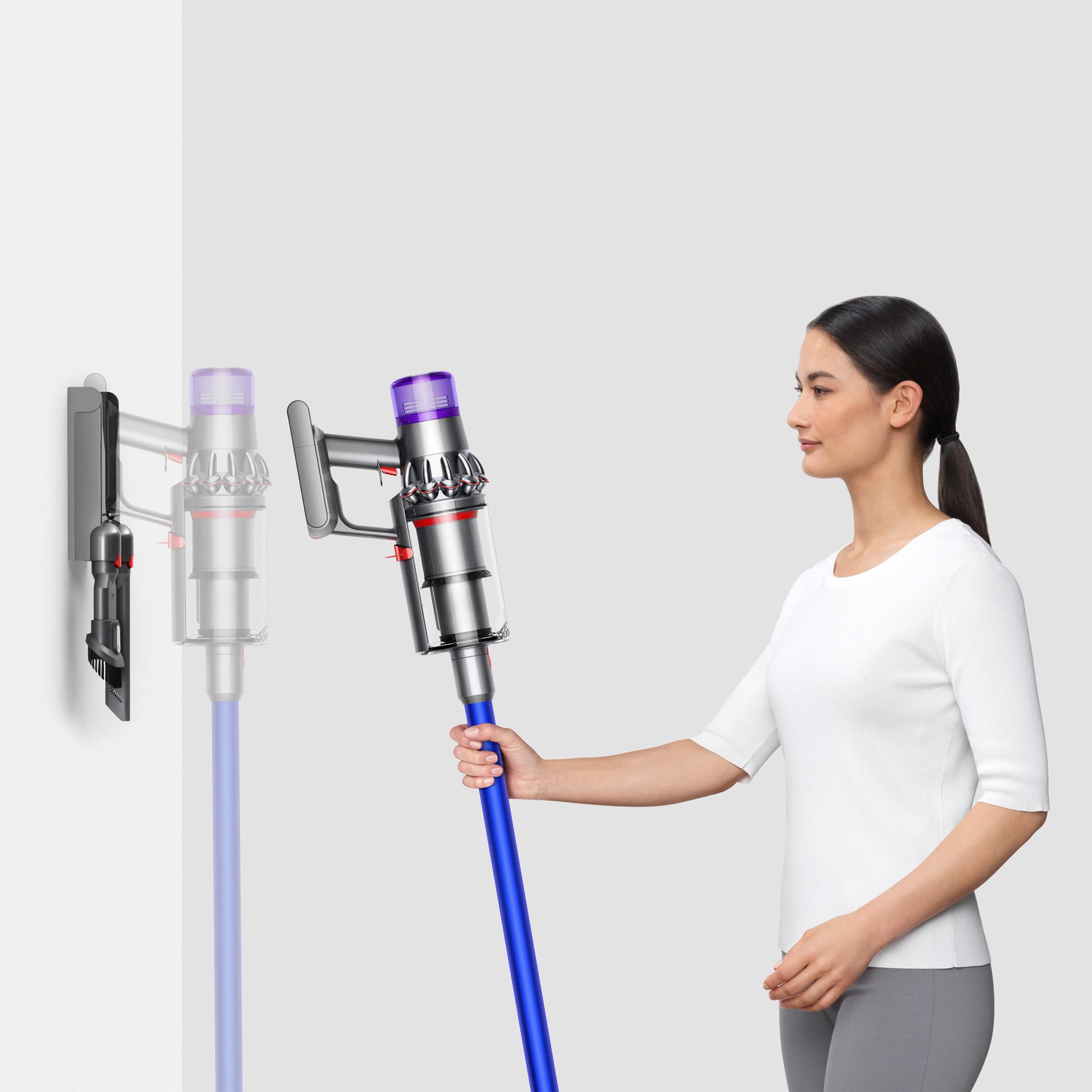 Eine Frau, die einen Dyson-Staubsauger in der Nähe einer Wandhalterung hält.