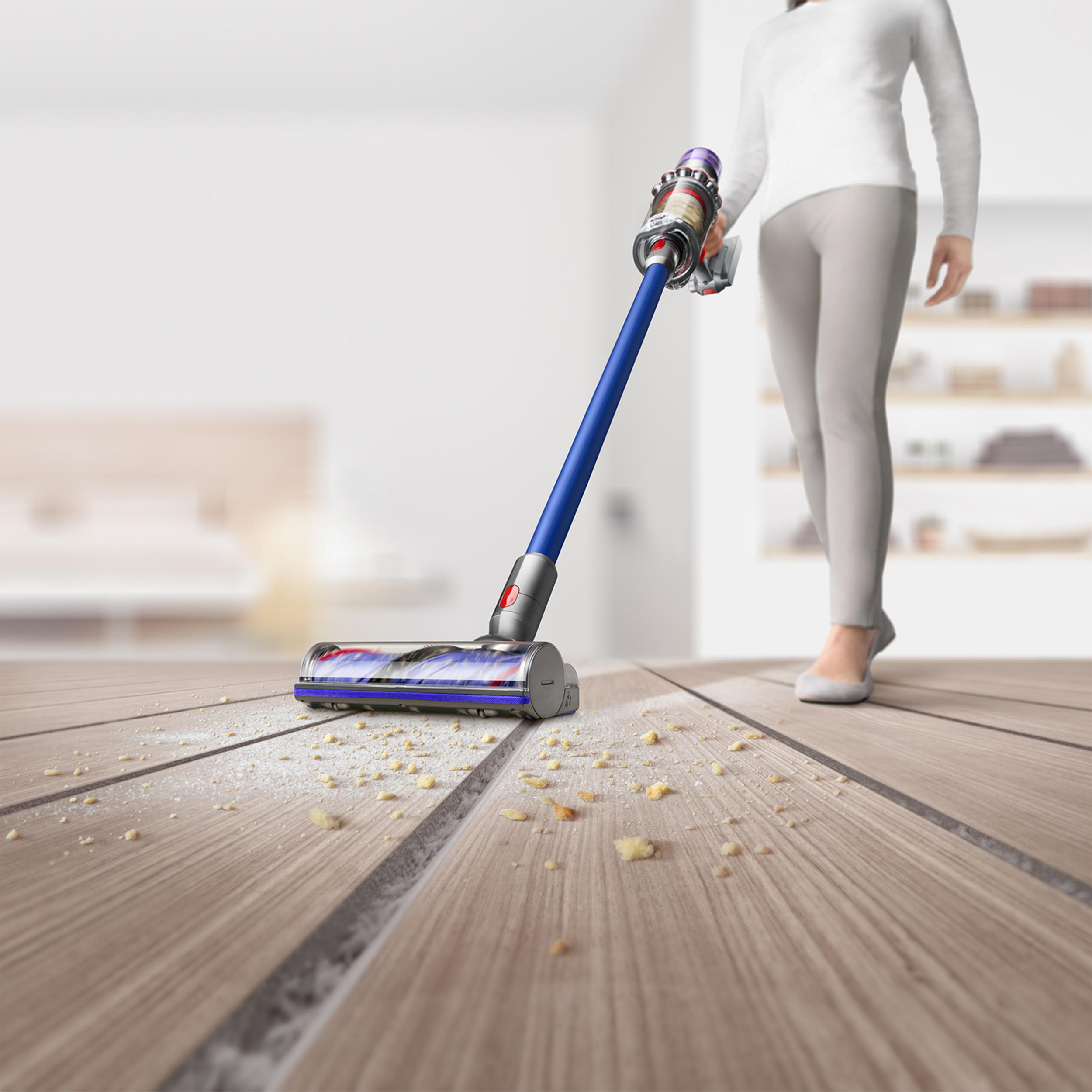 Eine Frau, die einen Holzboden mit einem blau-silbernen Staubsauger saugt, Staub ist sichtbar.