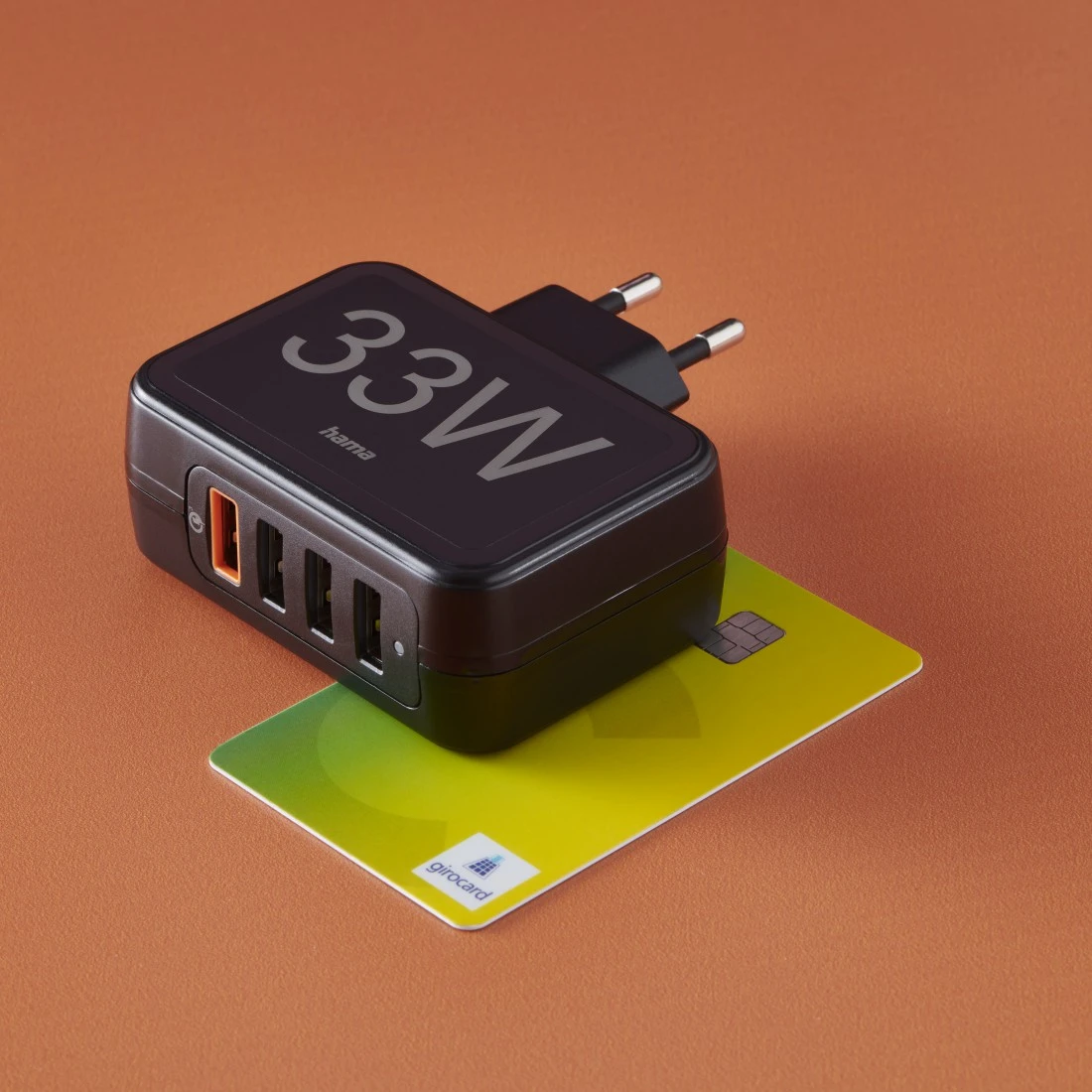 Ein schwarzes 33W Ladegerät mit Ladeanschluss und Kreditkarte auf braunem Untergrund.