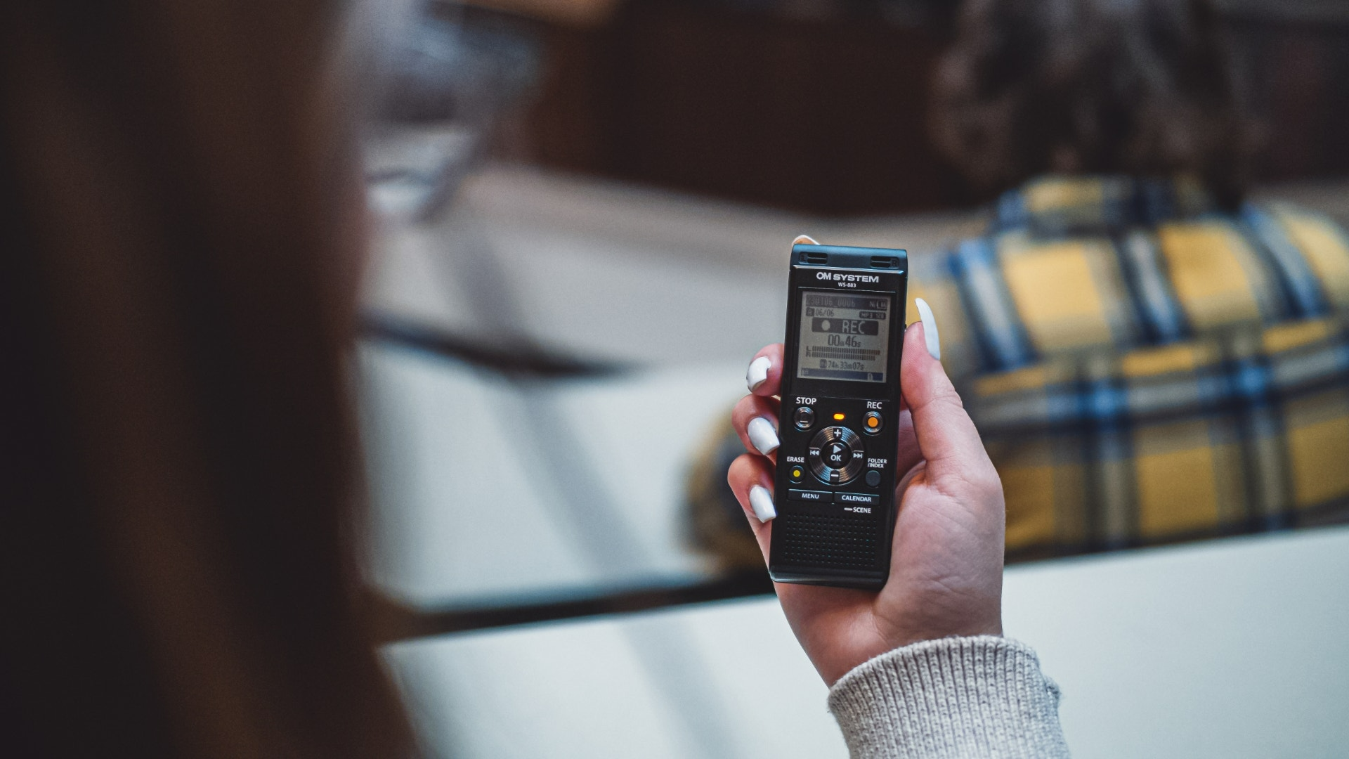 Egy személy egy fekete digitális hangrögzítőt tart. A képernyő a felvétel részleteit mutatja.