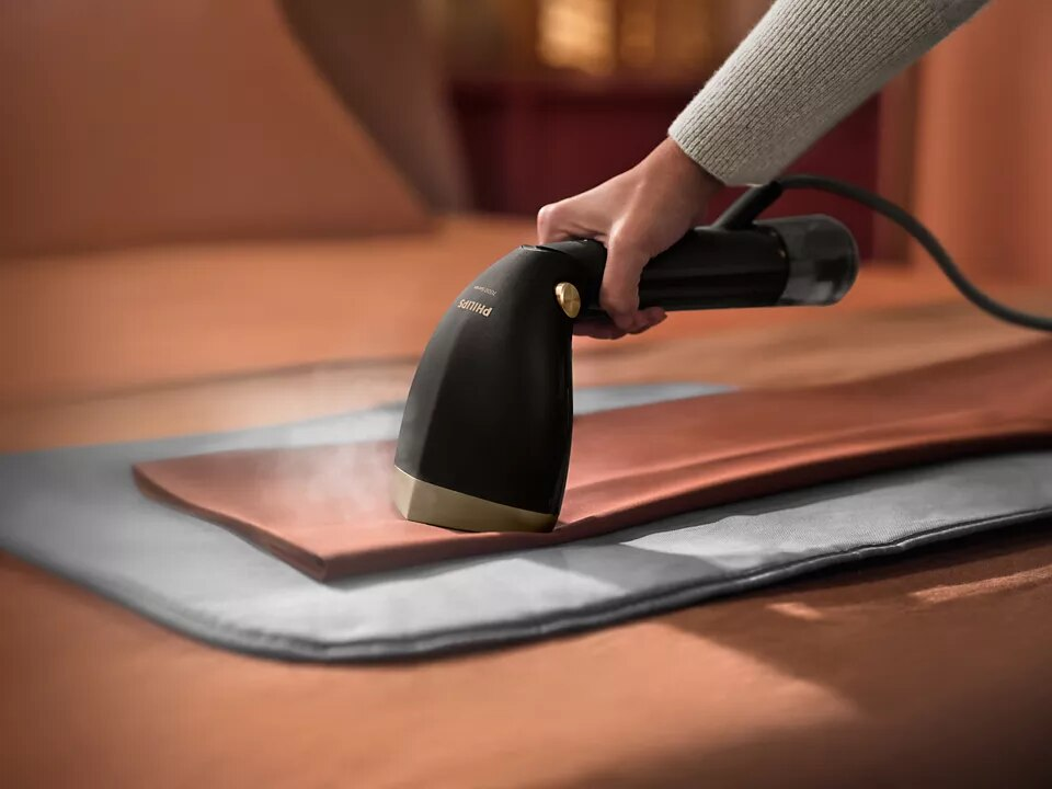 Ręka parująca brązowy skórzany przedmiot z czarno-złotym parownikiem Philips na szarej podkładce.