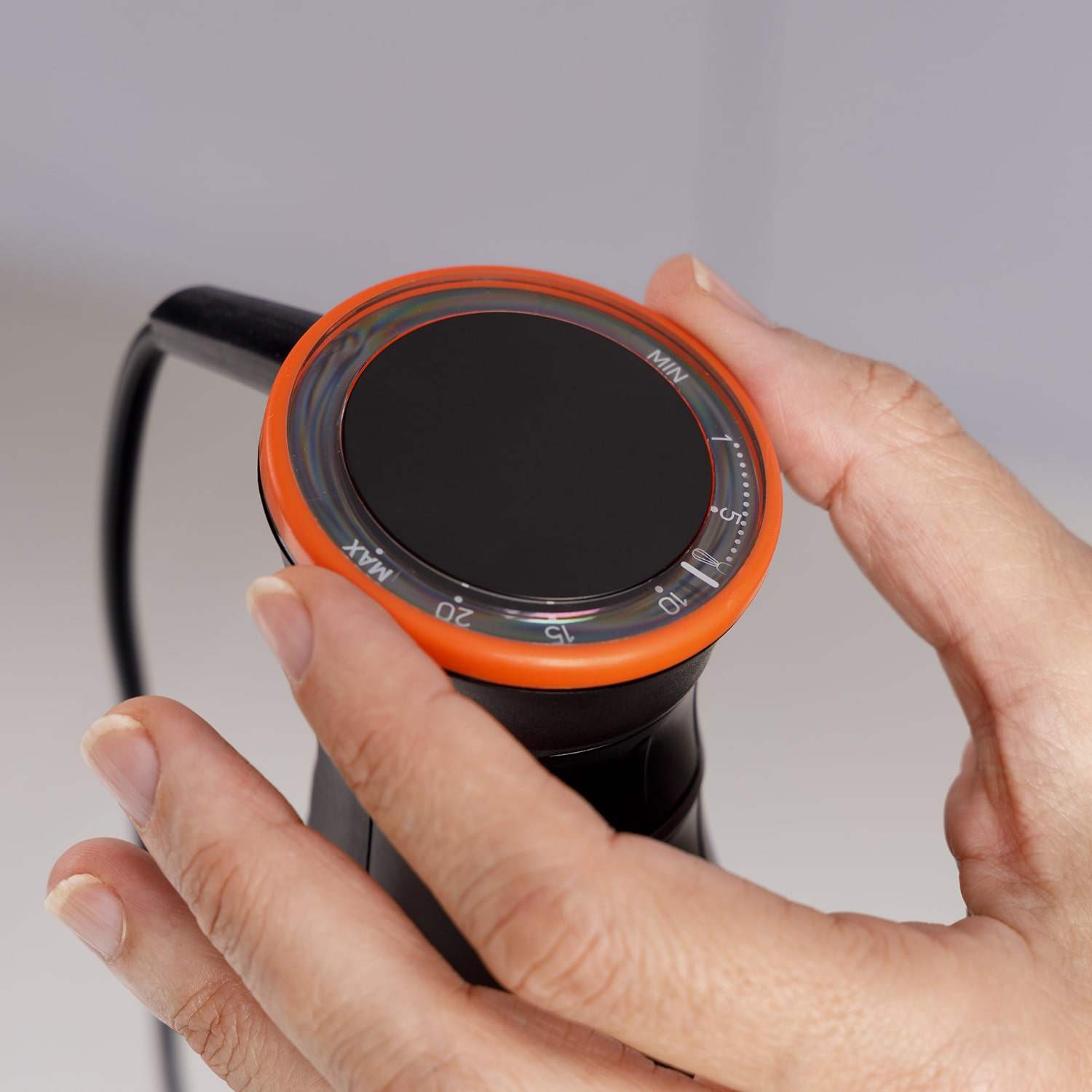 Una mano ajustando el dial de un control de temperatura negro y naranja.