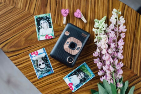 Aparat Instax ze zdjęciami i dekoracjami na drewnianej powierzchni. Kwiaty w tle.