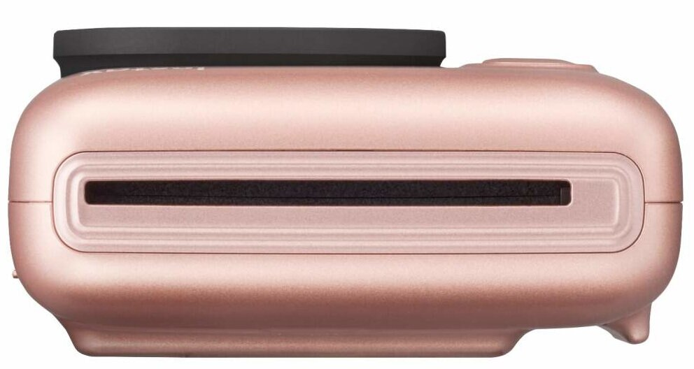 Aparat natychmiastowy w kolorze różowego złota, widok z boku, pokazujący gniazdo na film i czarną osłonę obiektywu.