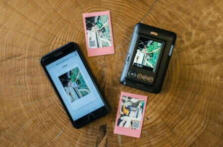 Telefon, aparat i dwa zdjęcia polaroid na drewnianym stole.