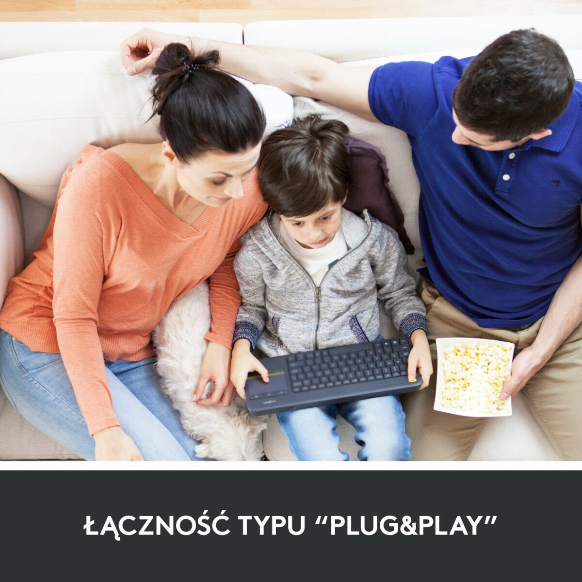 Rodzina na kanapie. Dziecko gra na klawiaturze. Jedzą popcorn.