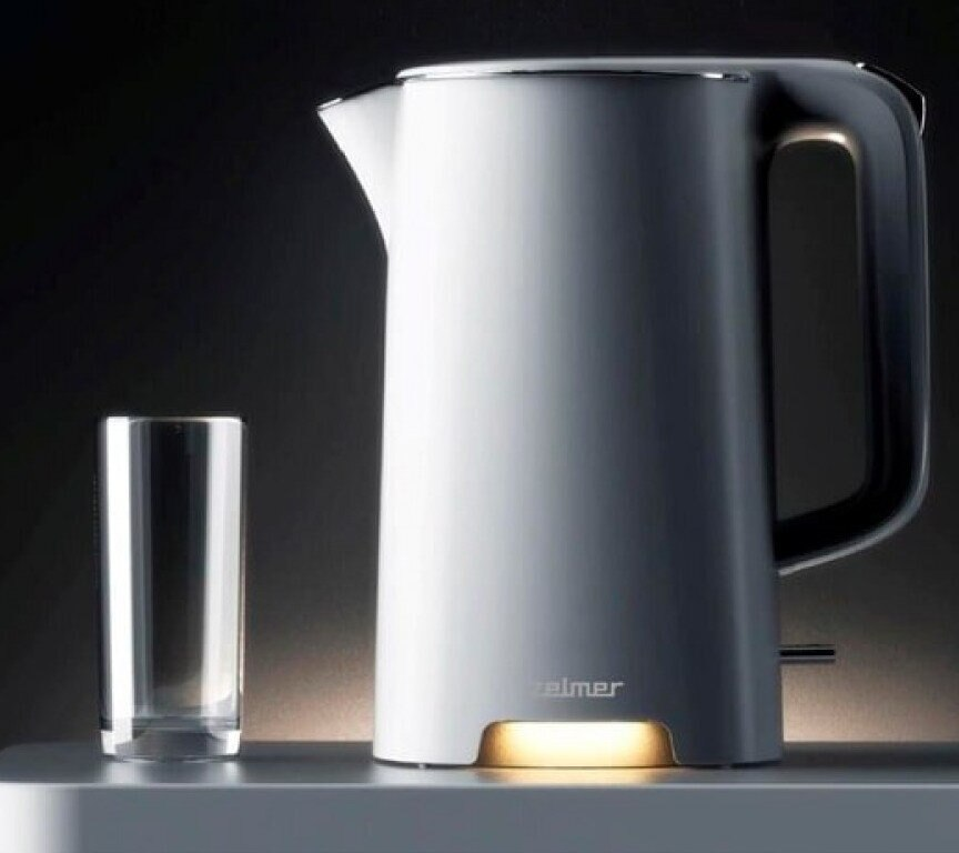 Biały czajnik elektryczny i szklanka, oba na białej powierzchni, na ciemnym tle.