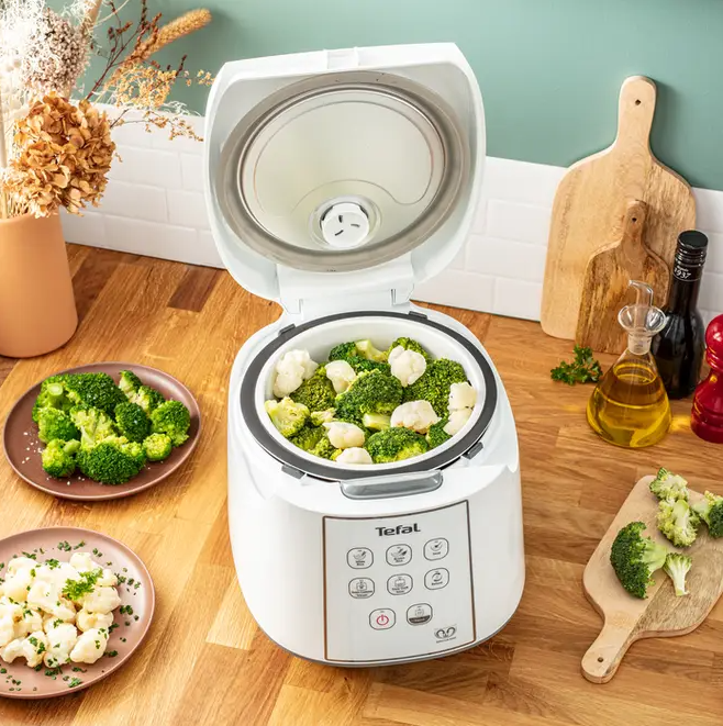 Weißer Tefal Reiskocher offen mit Brokkoli und Blumenkohl, auf einer Holzoberfläche.