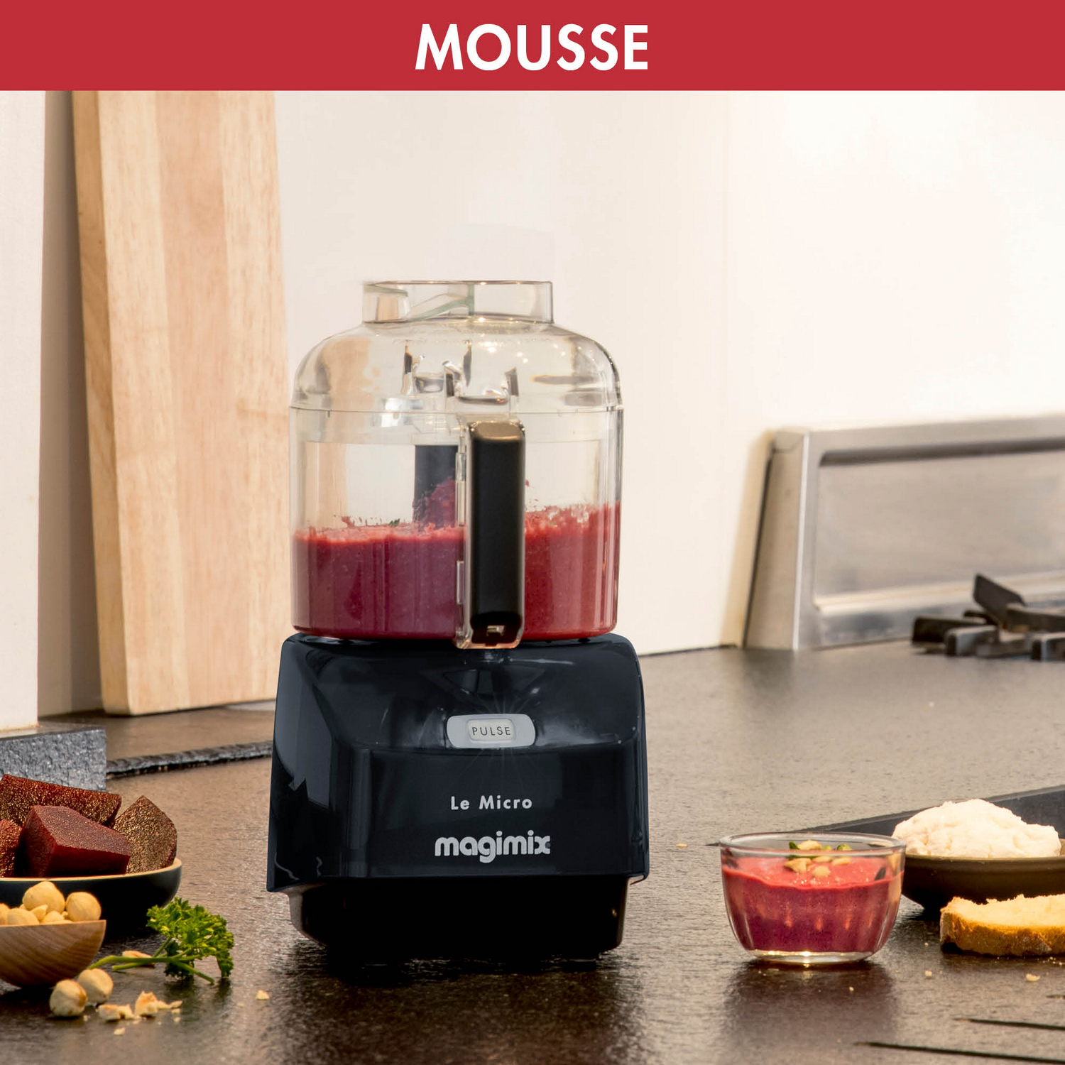 A food processor with red mousse inside, with ingredients and a bowl of mousse nearby.