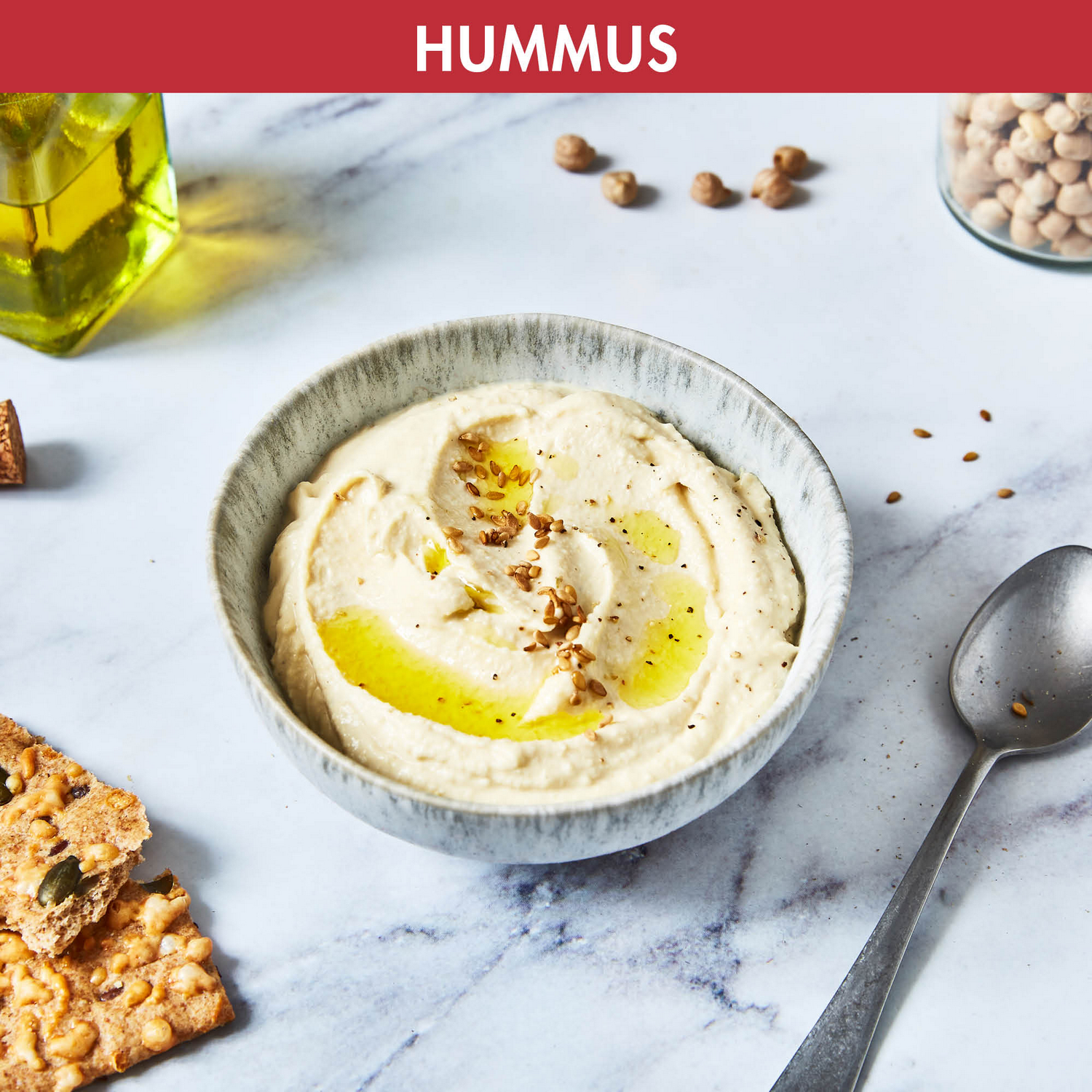 A bowl of hummus, garnished with olive oil and sesame seeds, on a marble surface.