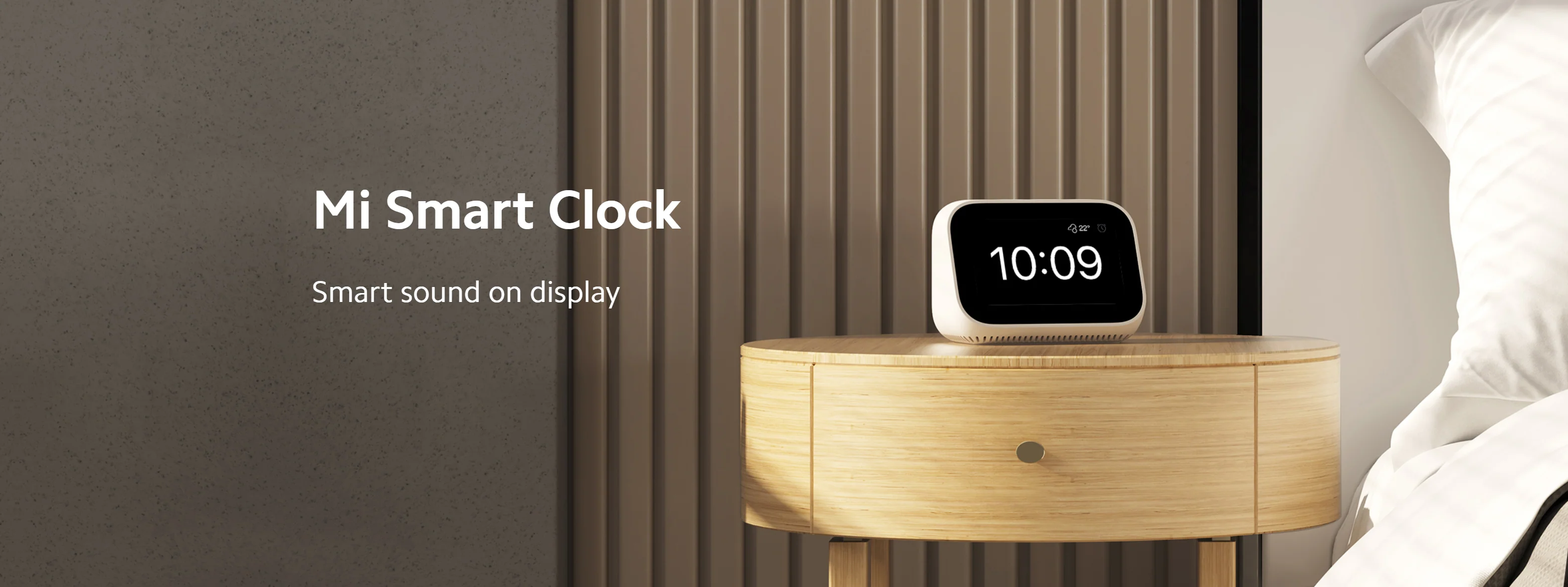 Mi Smart Clock su comodino in legno, visualizza l'ora 10:09. Biancheria da letto bianca dietro.