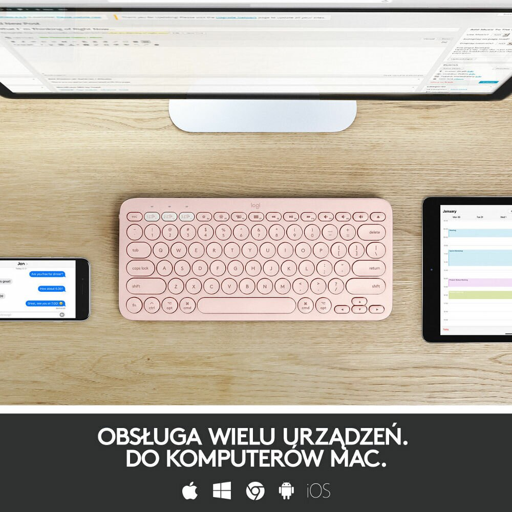 Różowa klawiatura bezprzewodowa, telefon i tablet na drewnianym biurku, tekst na dole.