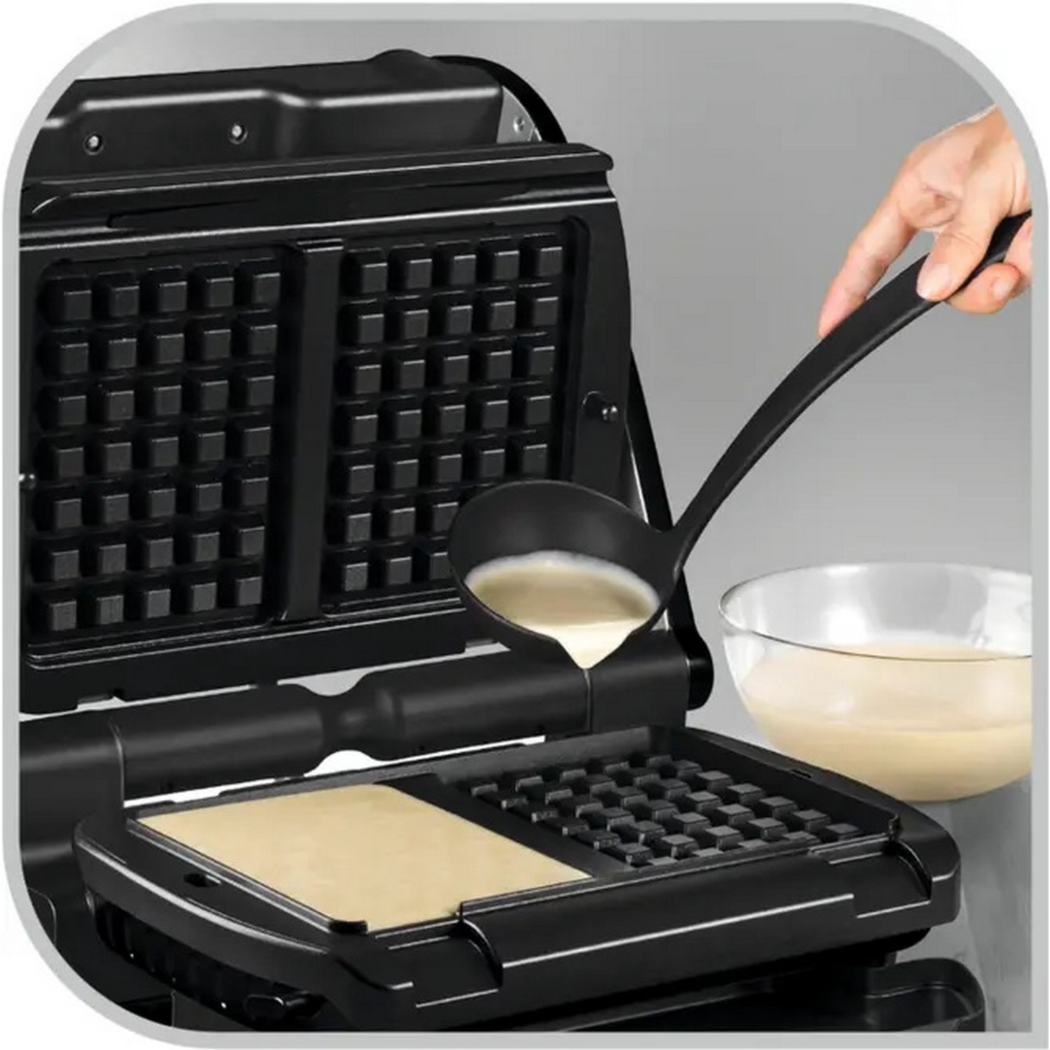 A person pours batter from a ladle into a waffle iron. One waffle is cooking.
